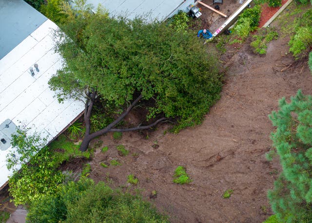 <p>This aerial view shows a man shovelling mud after a landslide pushed a tree into his and his neighbor's houses as the second and more powerful of two atmospheric river storms inundates the Hollywood Hills of Los Angeles, California, on February 5, 2024</p>