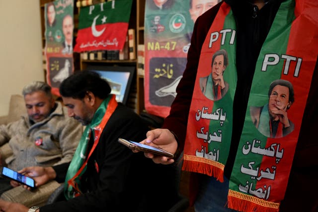 <p>Pakistan's former prime minister Imran Khan's supporters wear scarves with prints of his Pakistan Tehreek-e-Insaf (PTI) party</p>