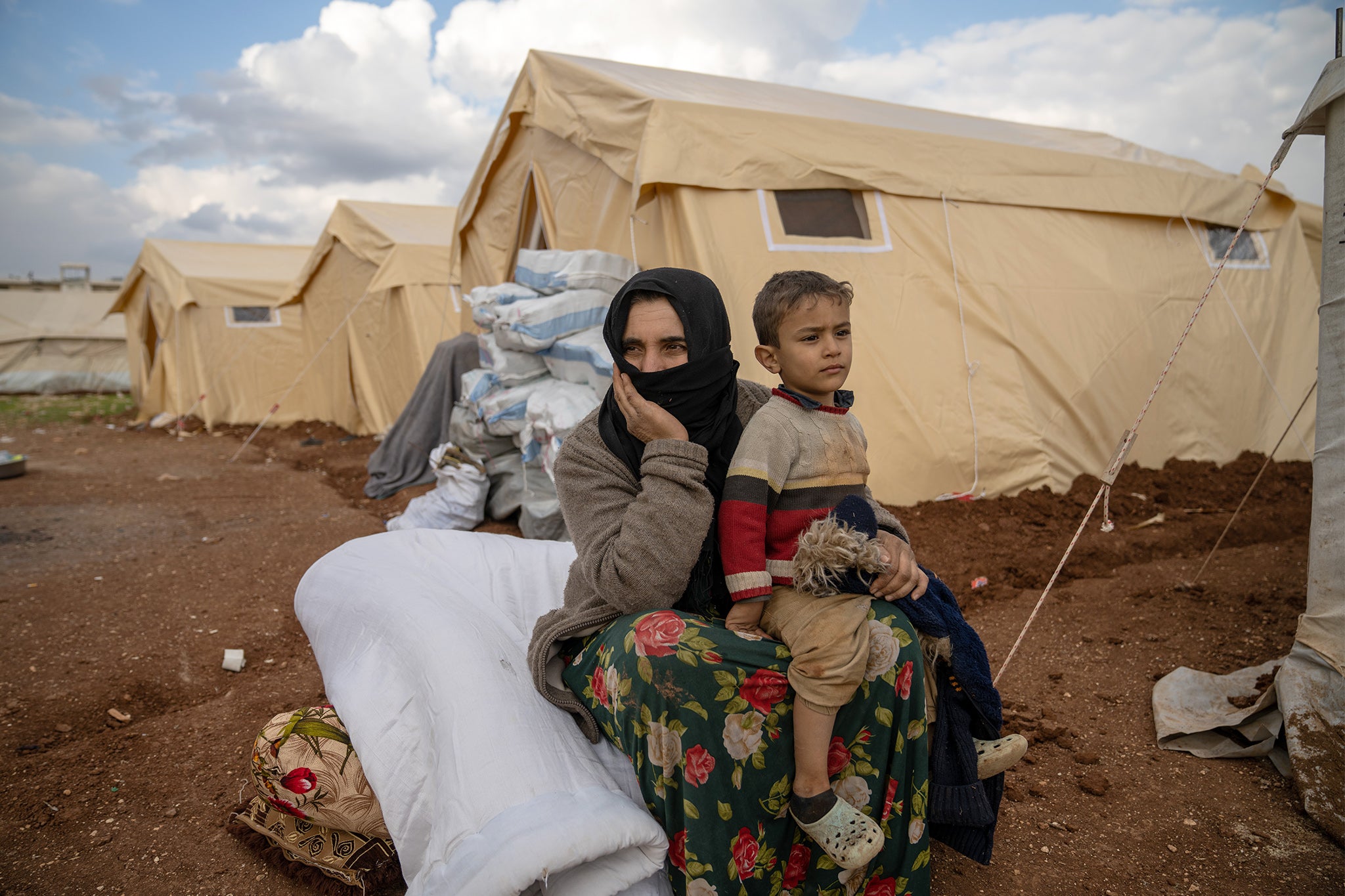 Amal* sits with her son in front of a tent in Jenderes, Syria