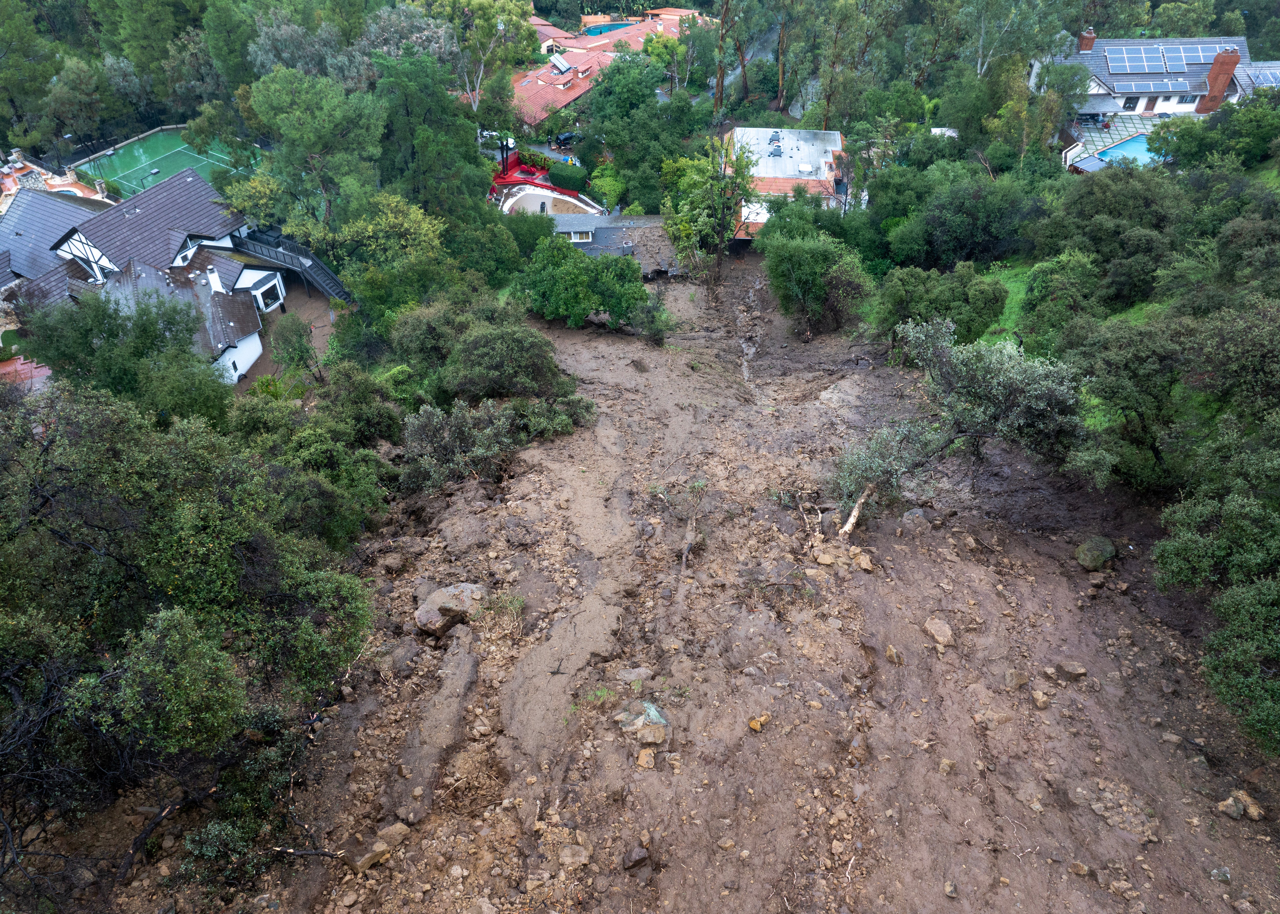 In an aerial view, a mudslide leads to a home where it smashed through its garage as a historic atmospheric river storm inundates the Studio City section of Los Angeles
