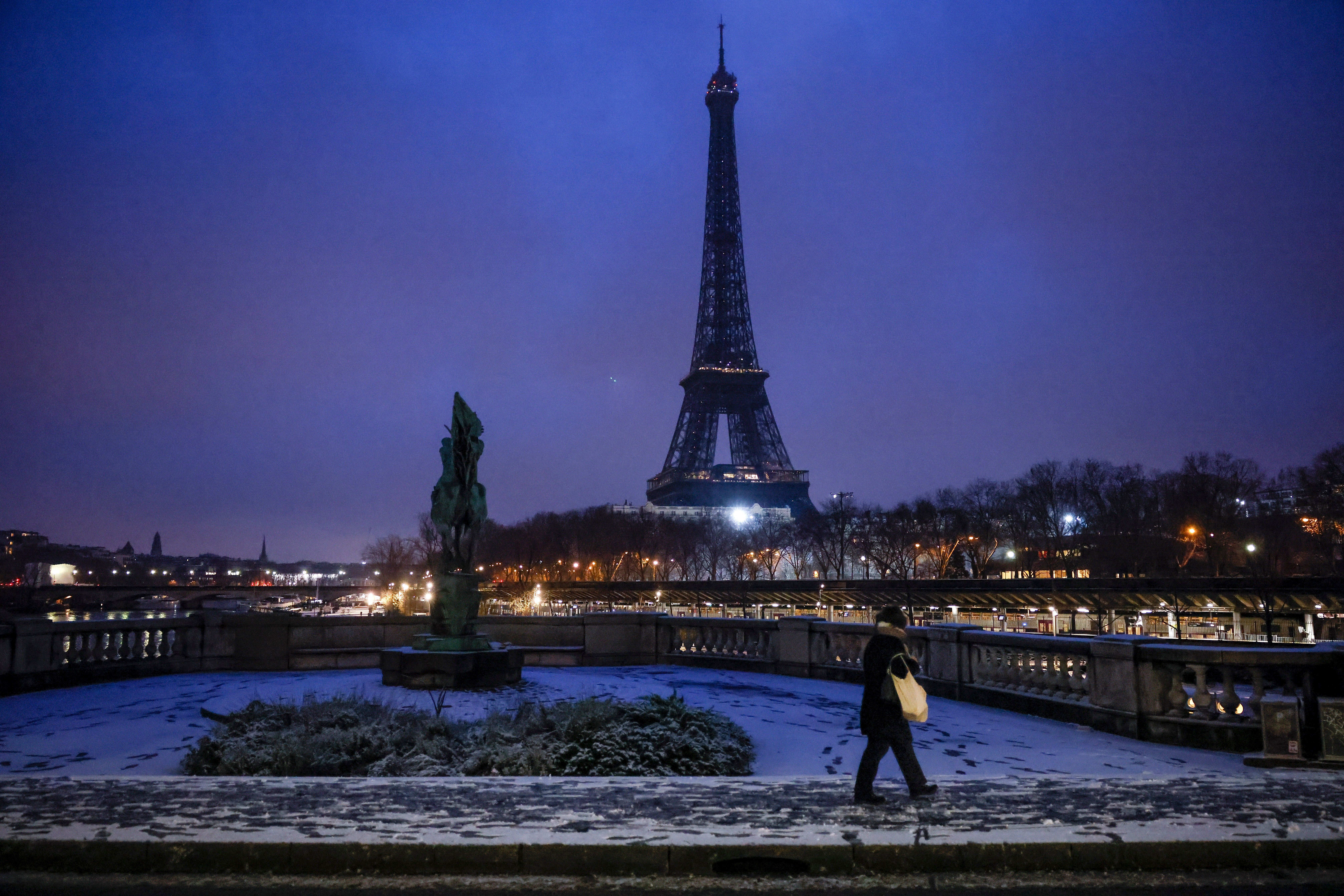 A woman walks to a bridge in front of the Eiffel Tower after snowfalls