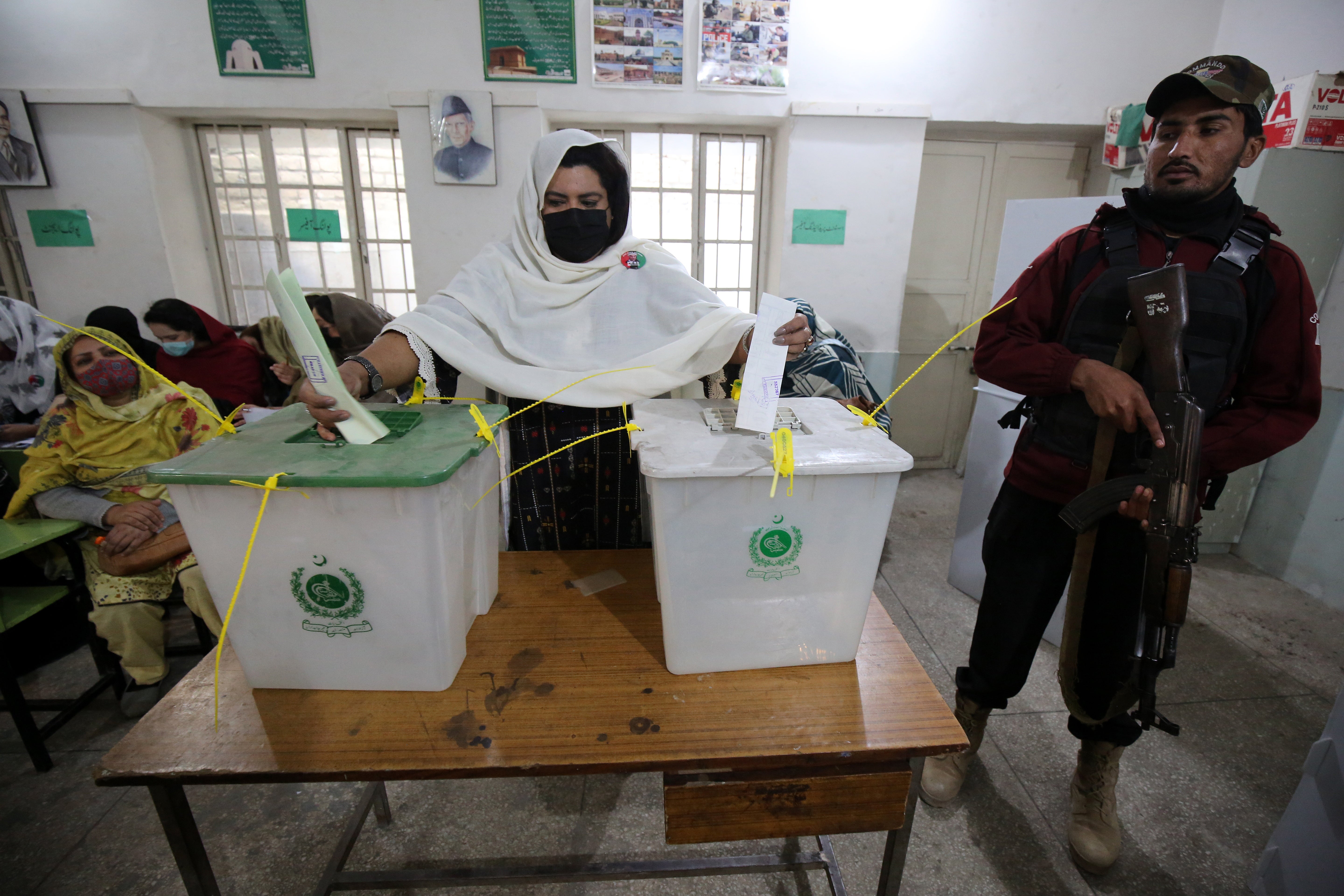 A policeman stands guard as a woman cast their ballot at a polling station during general elections in Peshawar