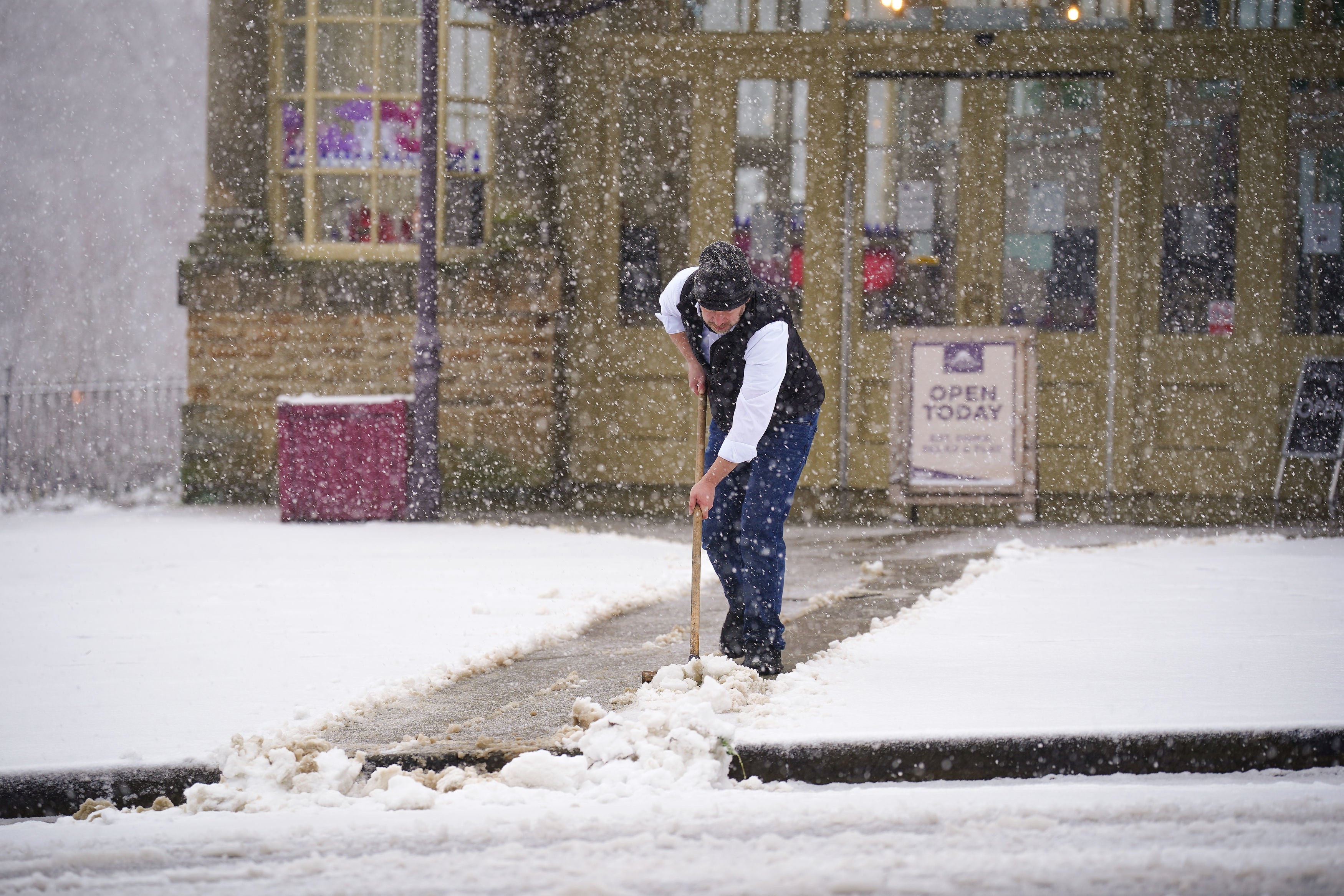 A person clears snow in front of the Opera House in Buxton, Peak District.