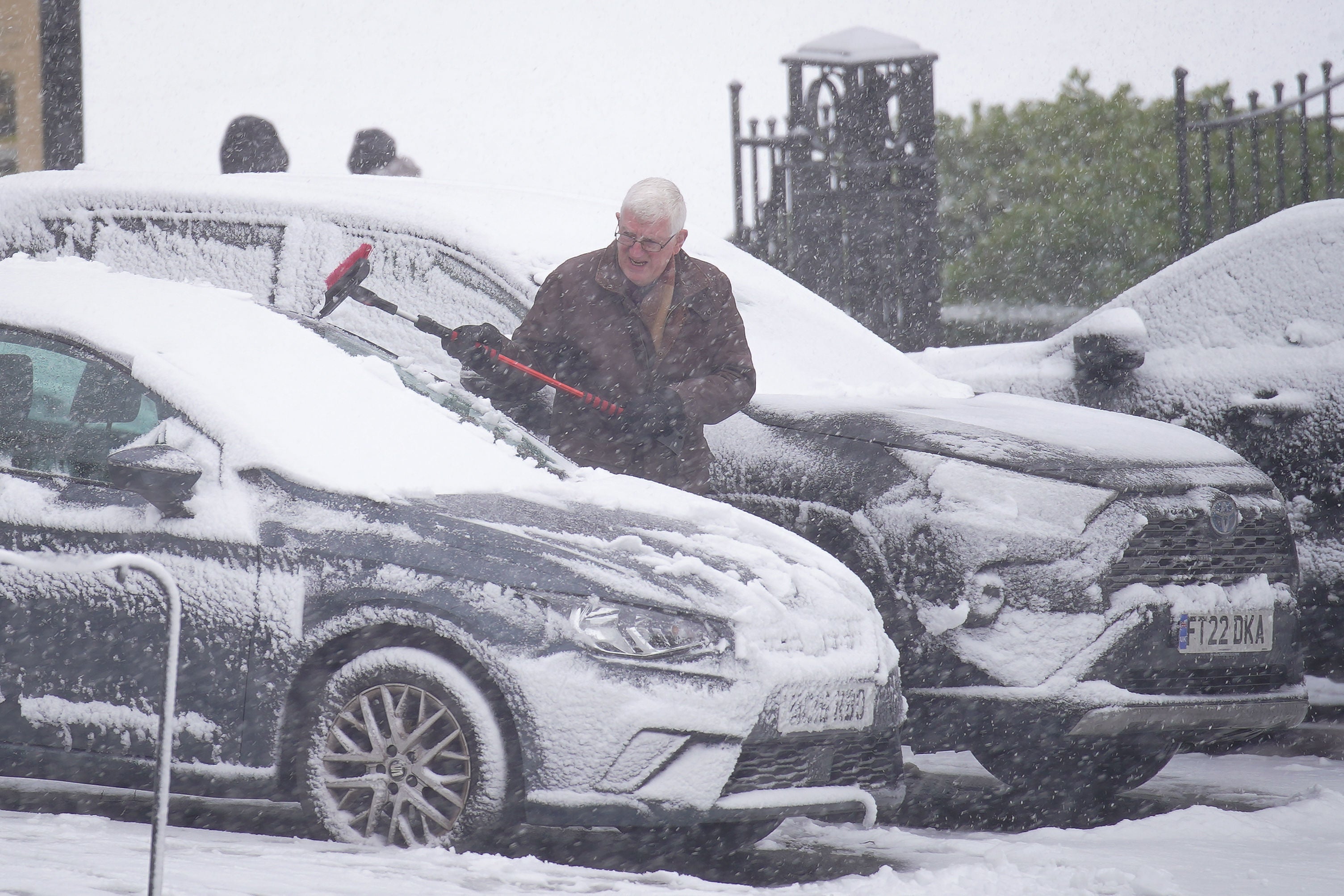A person clears snow from a parked car in Buxton, Peak District