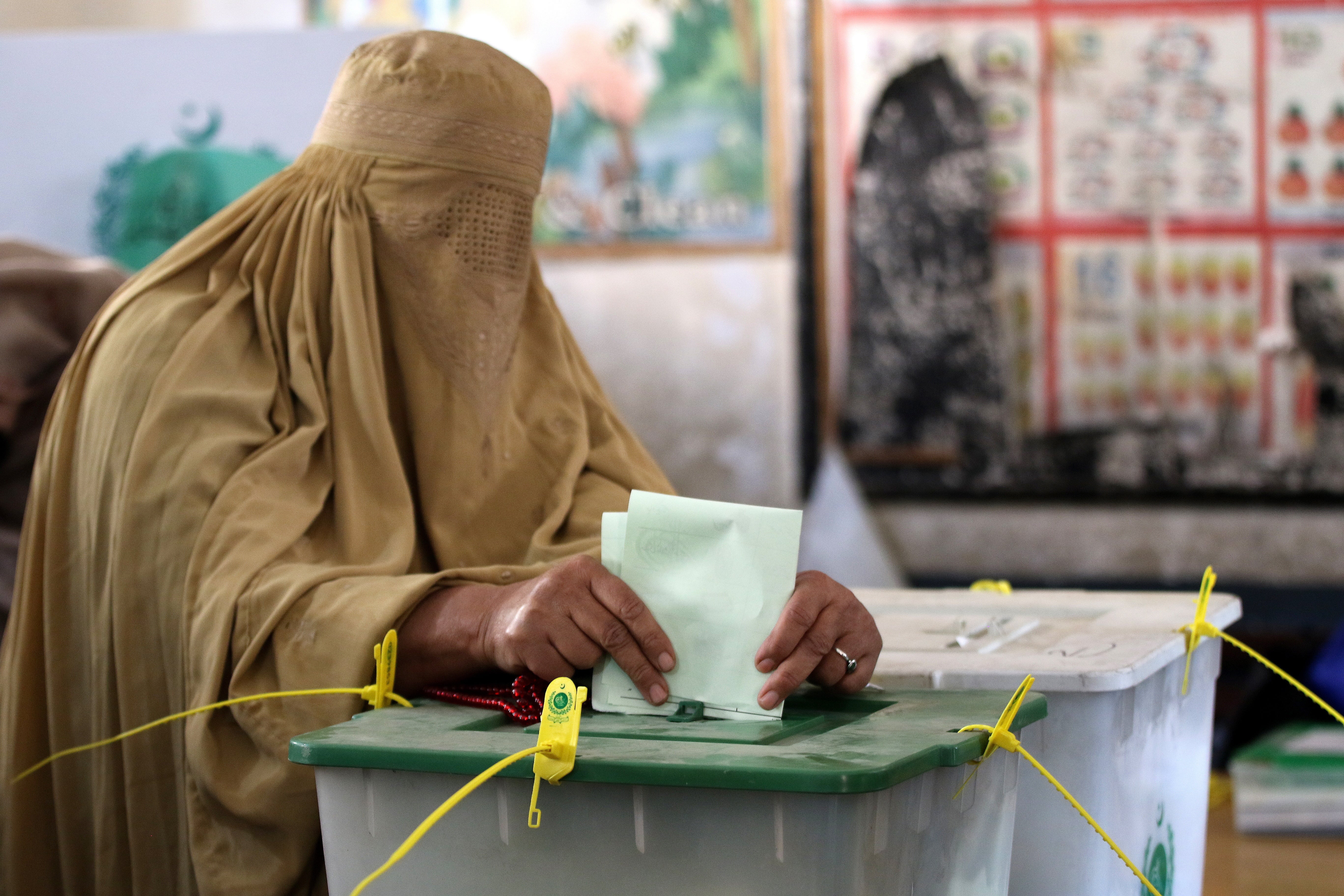 A Burqa-clad woman casts her ballot paper at a polling station during general elections in Peshawar