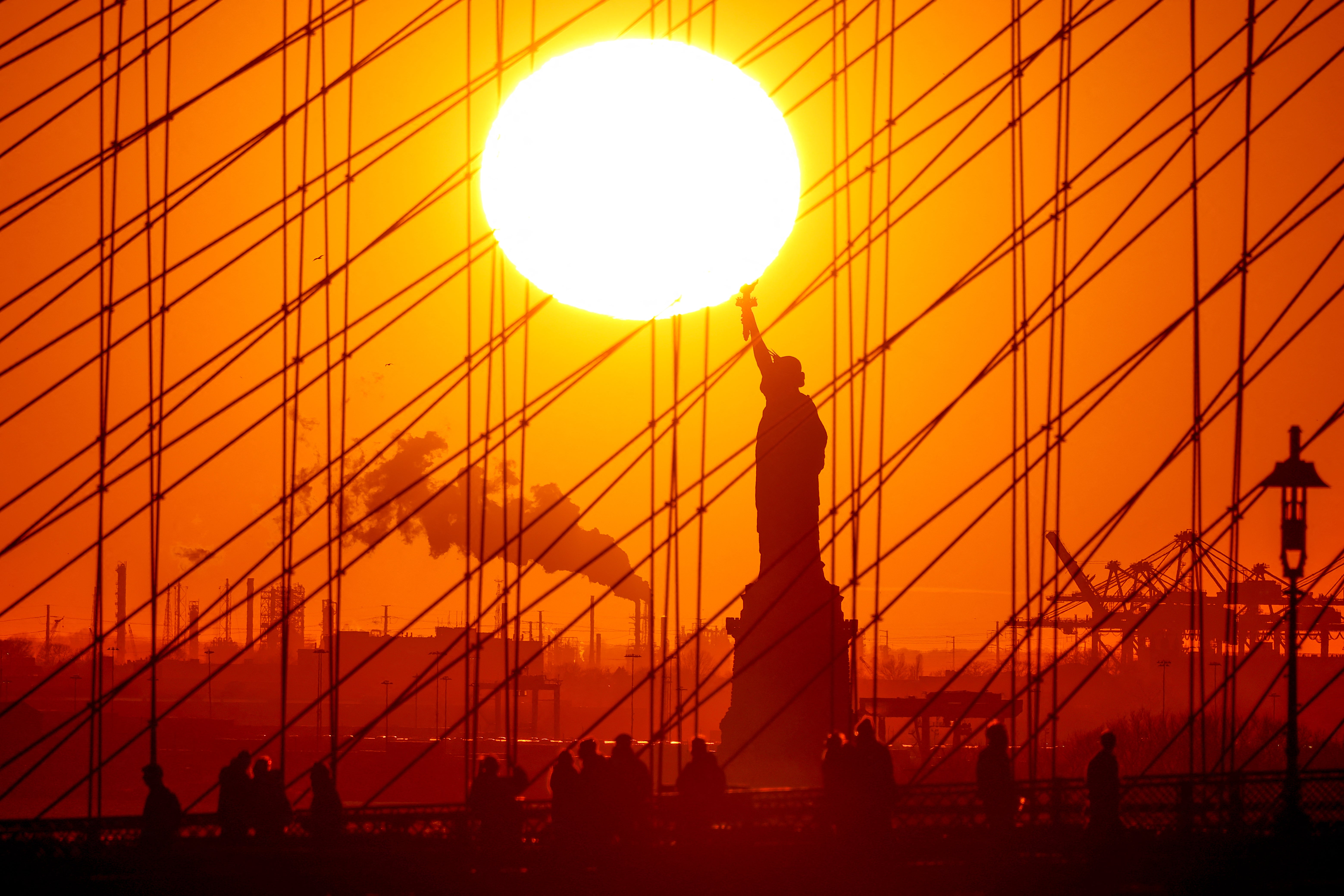 The sun sets behind the Statue of Liberty