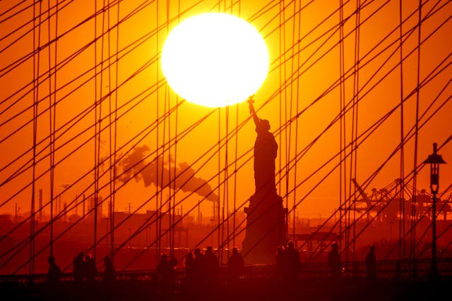 <p>The sun sets behind the Statue of Liberty </p>