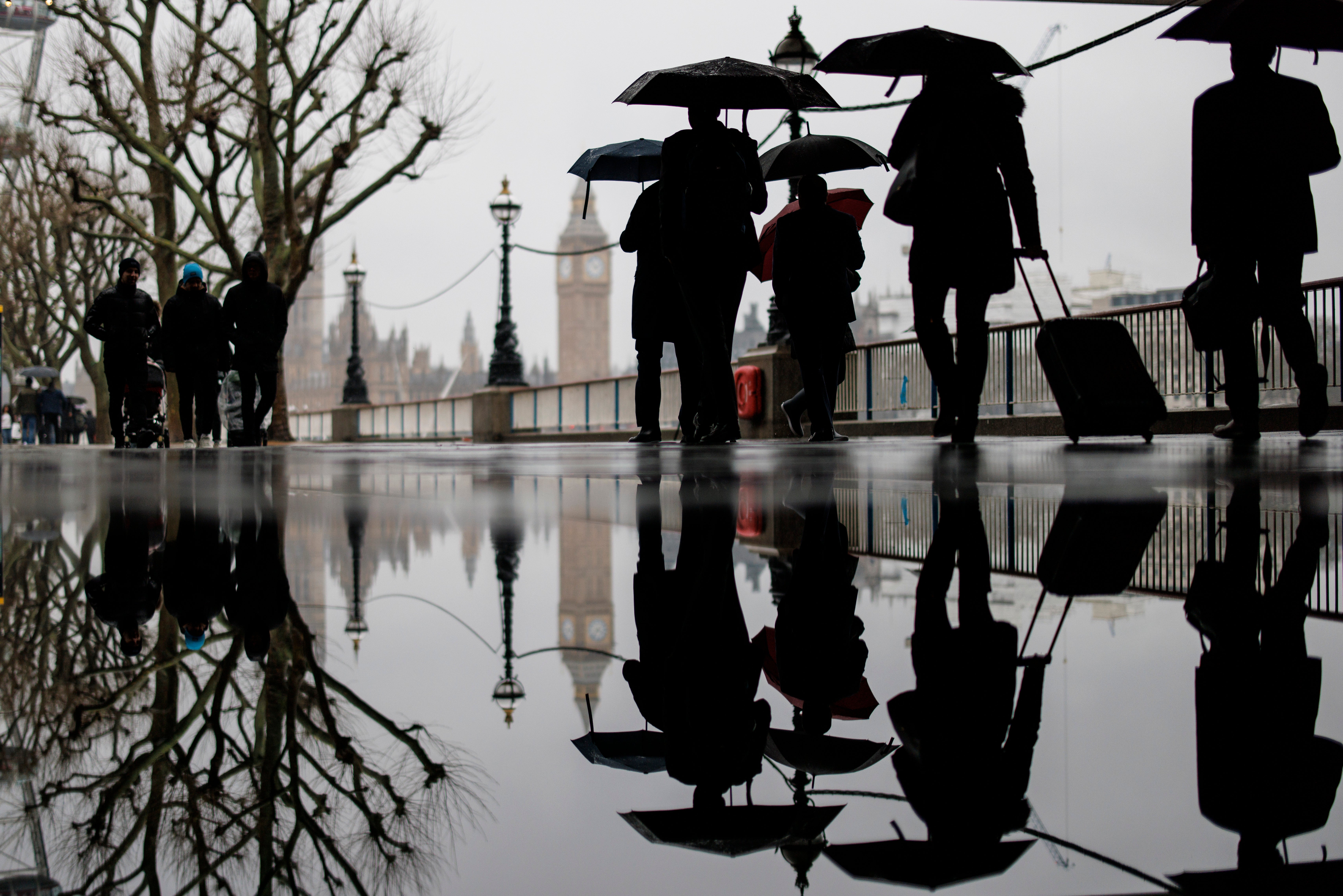 People walk past a puddle as they walk along the Southbank in the rain
