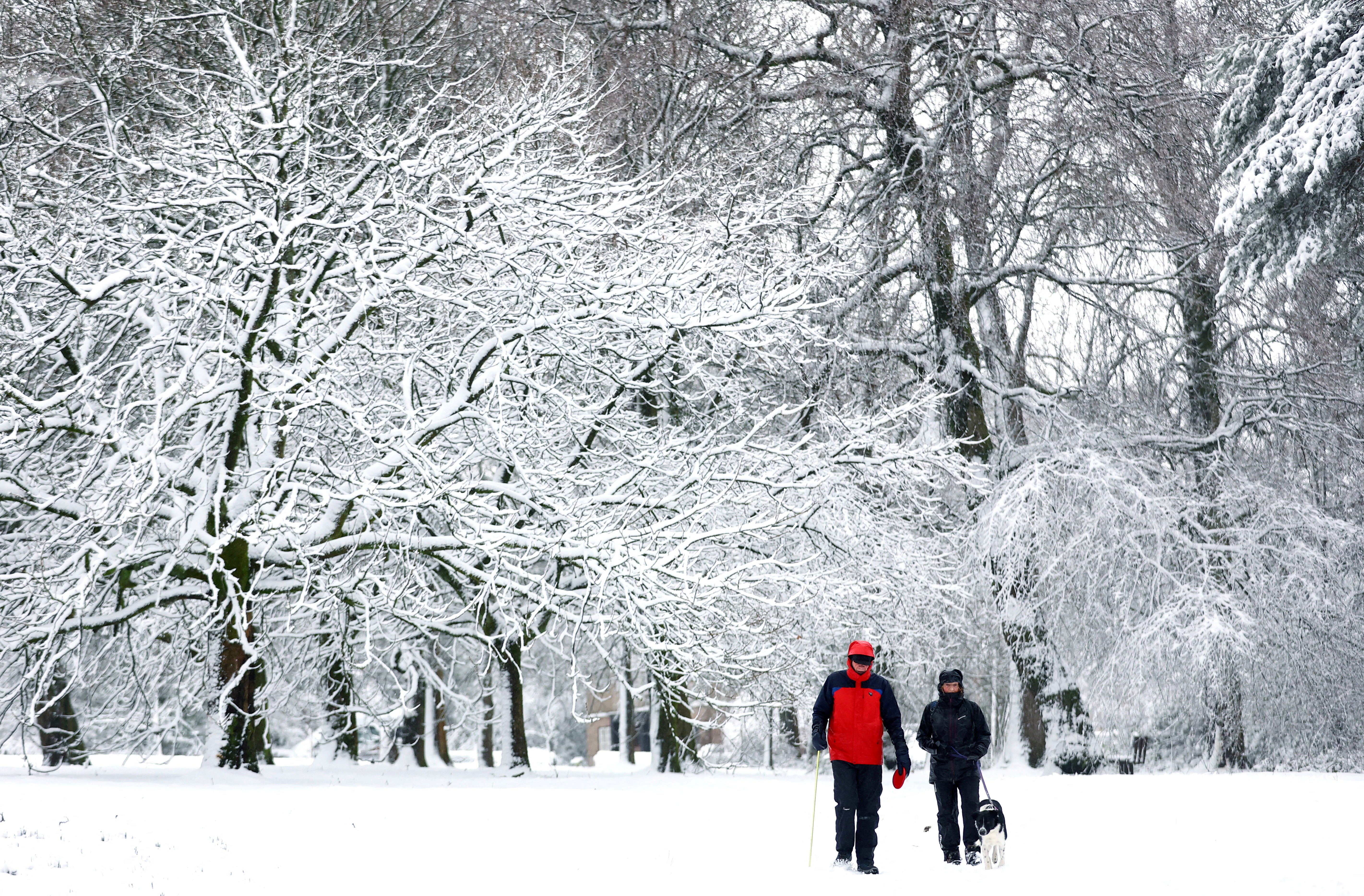 People walk their dog through a snow covered park in Buxton