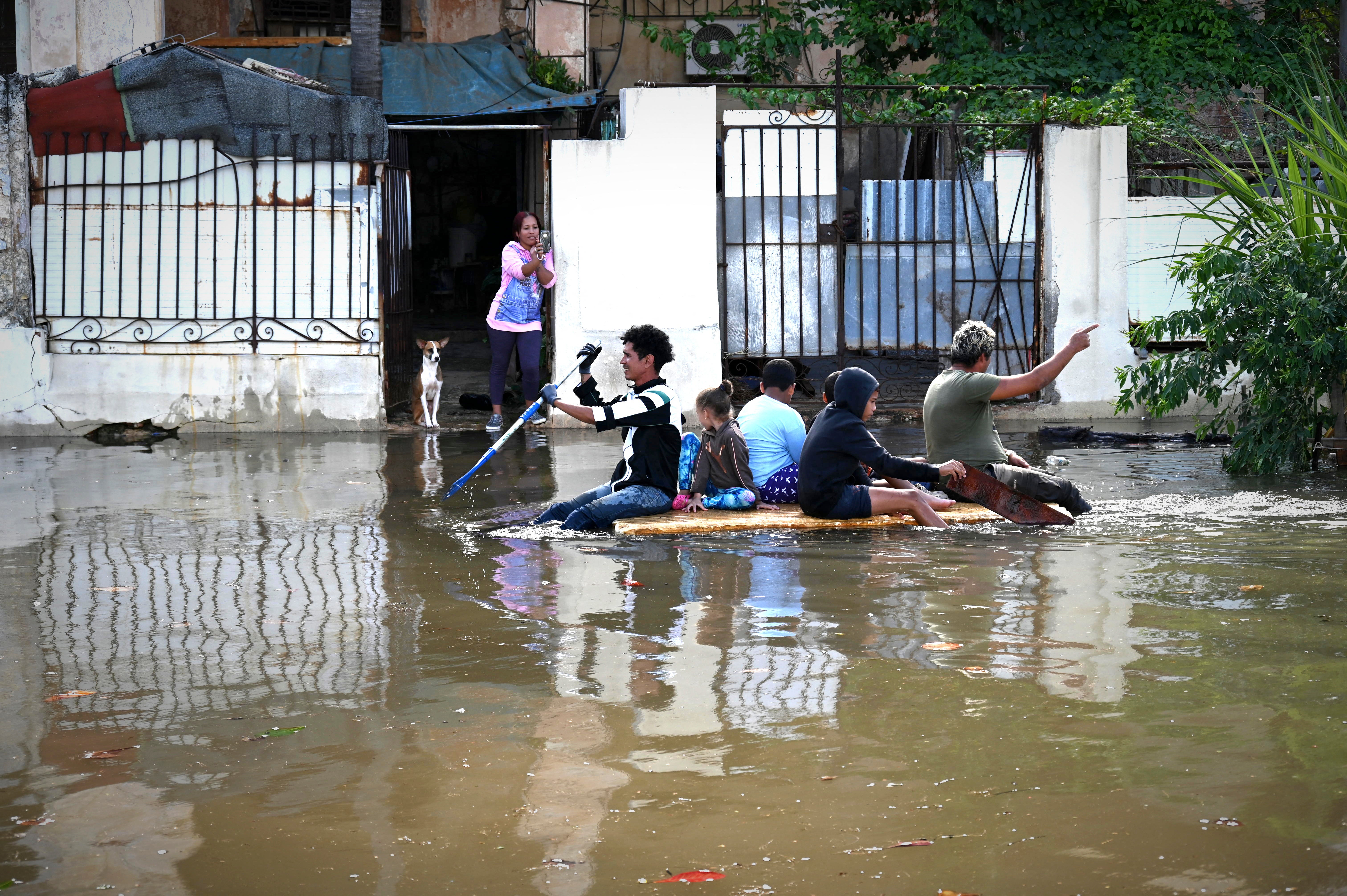 People navigate through a flooded street on a rustic raft in Havana