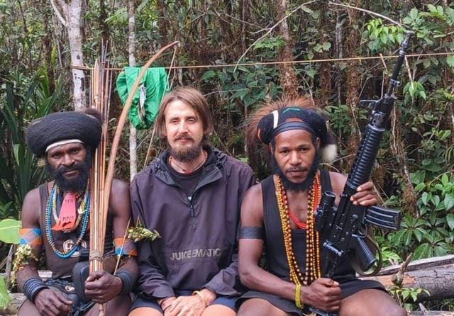 <p>Philip Mark Mehrtens, 38, sits inbetween two West Papua Liberation Army soldiers after he was captured last year </p>