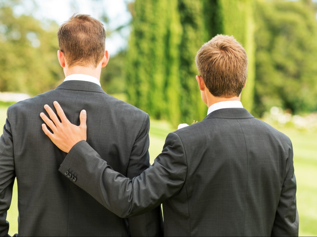 <p>Rear view of best man standing with hand on groom’s back in garden.</p>