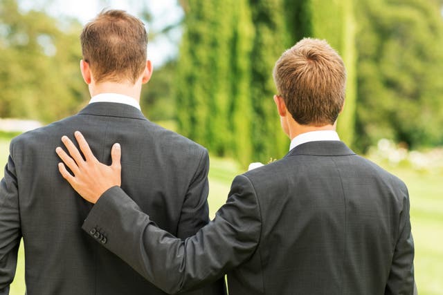 <p>Rear view of best man standing with hand on groom’s back in garden.</p>