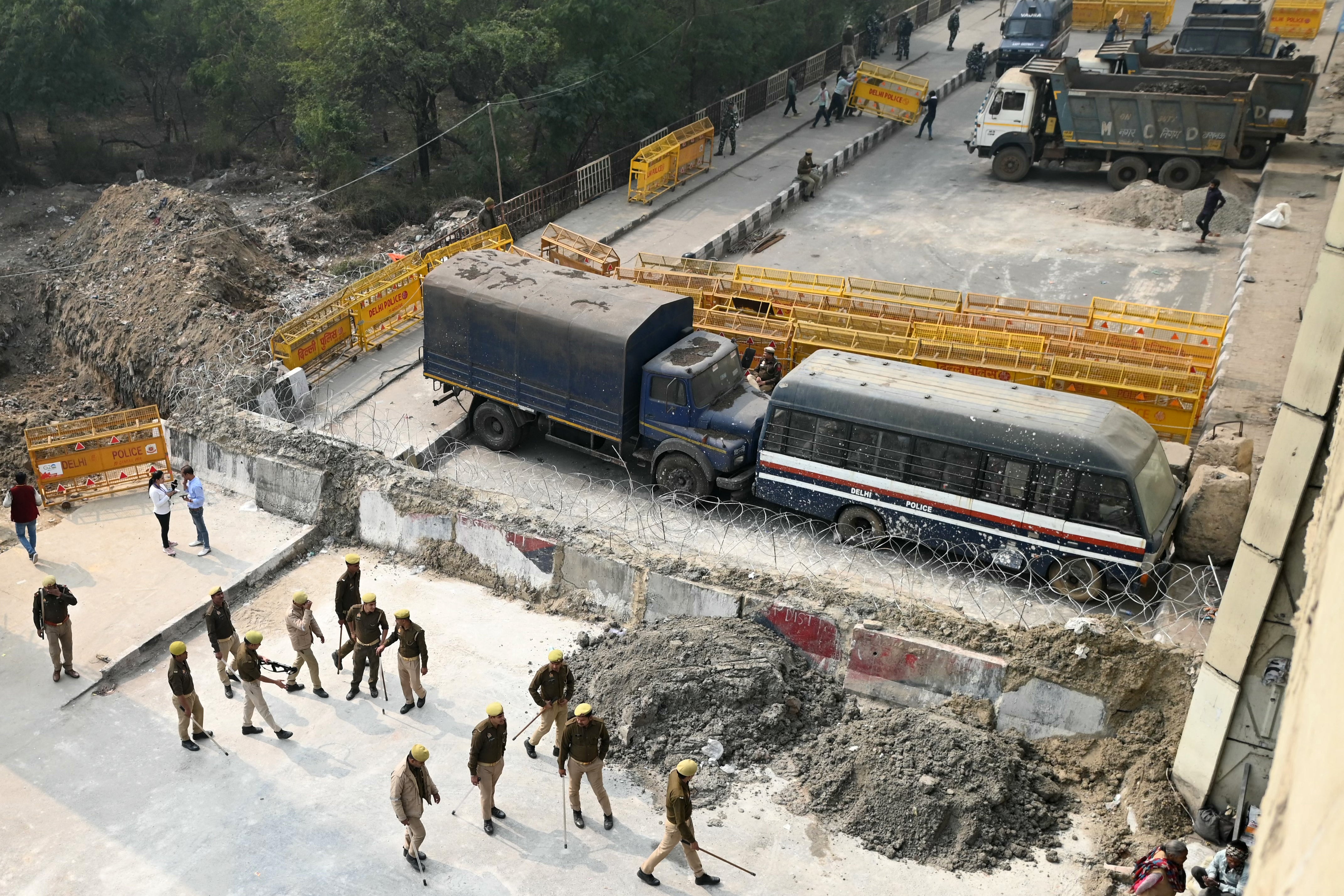 Police personnel stand guard next to a barrier and vehicles blocking a road to prevent farmers protesting to demand minimum crop prices from marching towards India’s capital at the Delhi-Uttar Pradesh border in Ghazipur