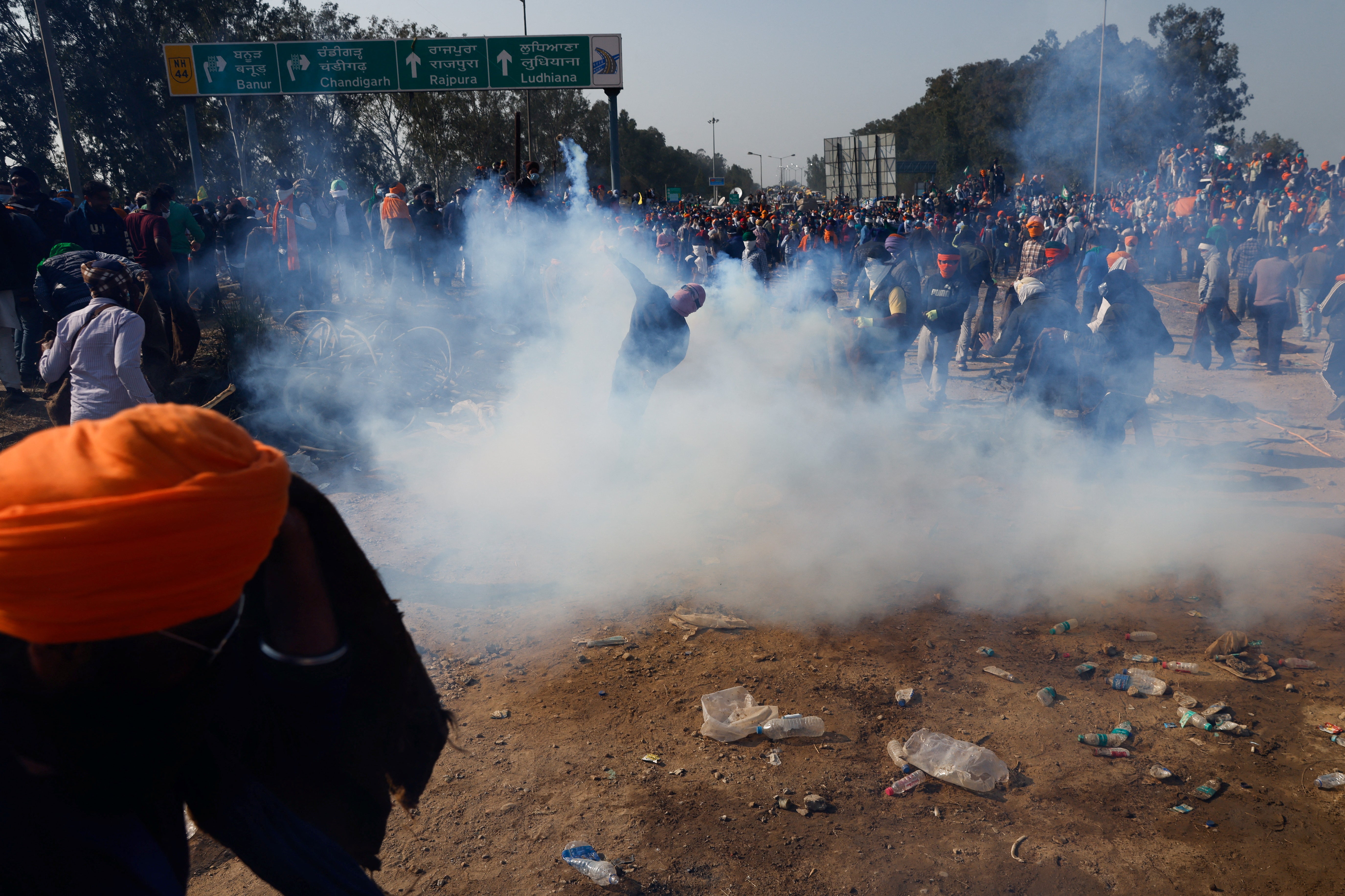 <p>People stand to throw jute bags at tear gas fired by the police to disperse farmers marching towards New Delhi to press for better crop prices promised to them in 2021, at Shambhu, a border crossing between Punjab and Haryana states, India, February 14, 2024</p>