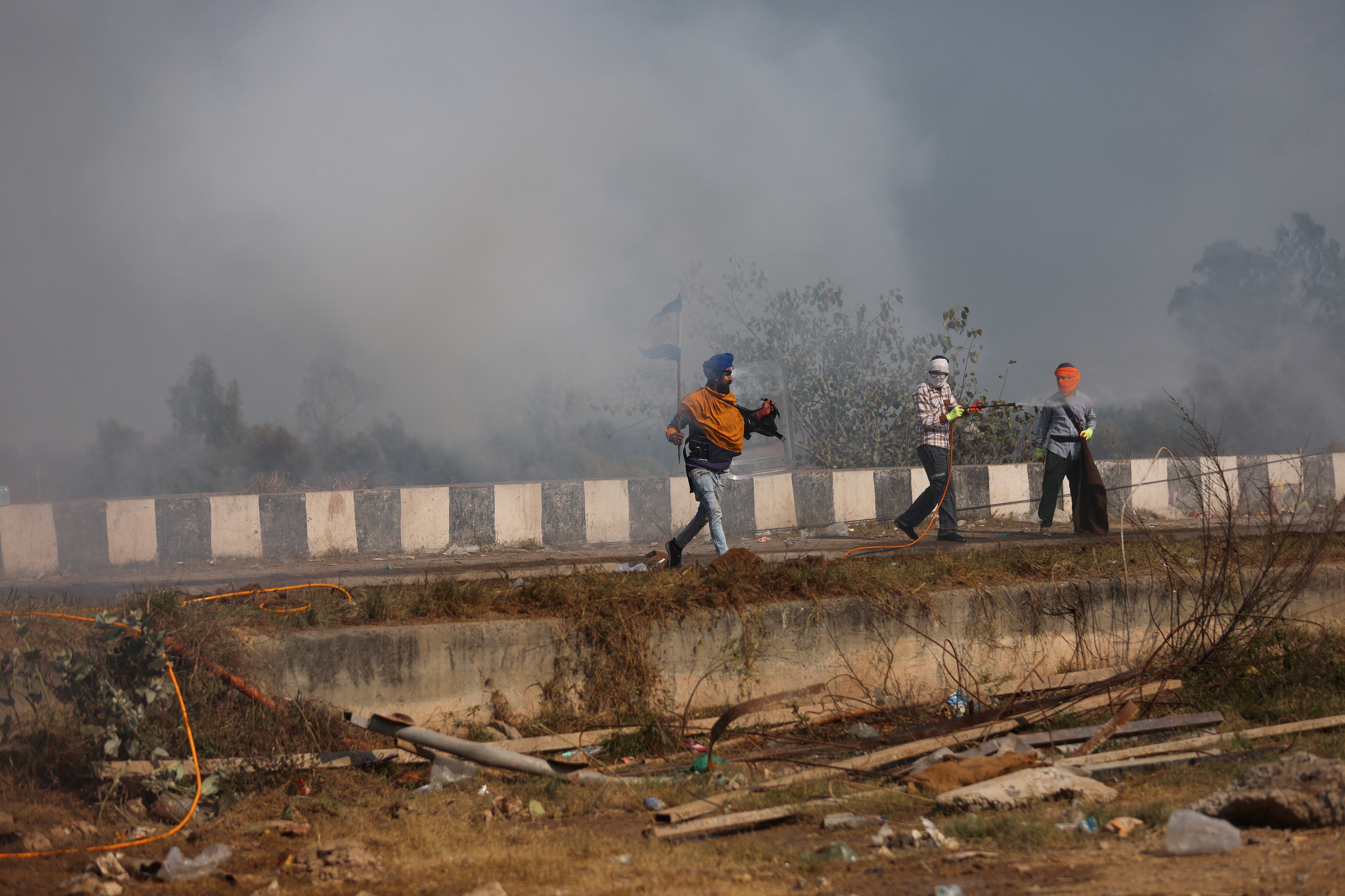 People stand amidst tear gas fired by police to disperse farmers who are marching towards New Delhi