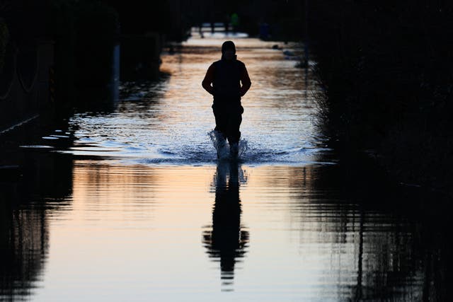 <p>File image: A person walks through a flooded road in Wraysbury, west of London during flooding in January. Met Office forecasts more rain is set to fall on saturated grounds potentially leading to floods</p>