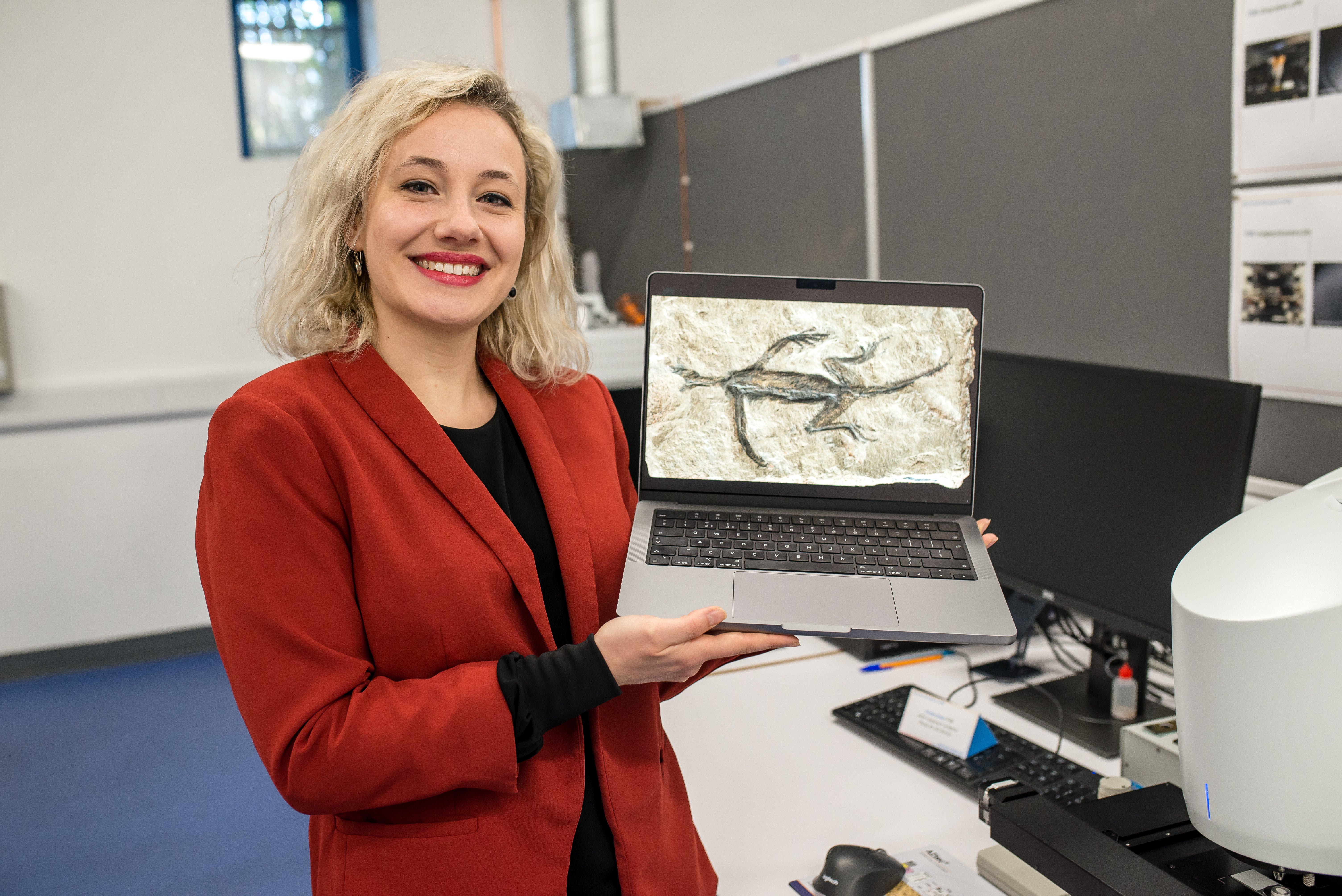 Dr Valentina Rossi with an image of Tridentinosaurus antiquus as the 280-million-year-old reptile fossil