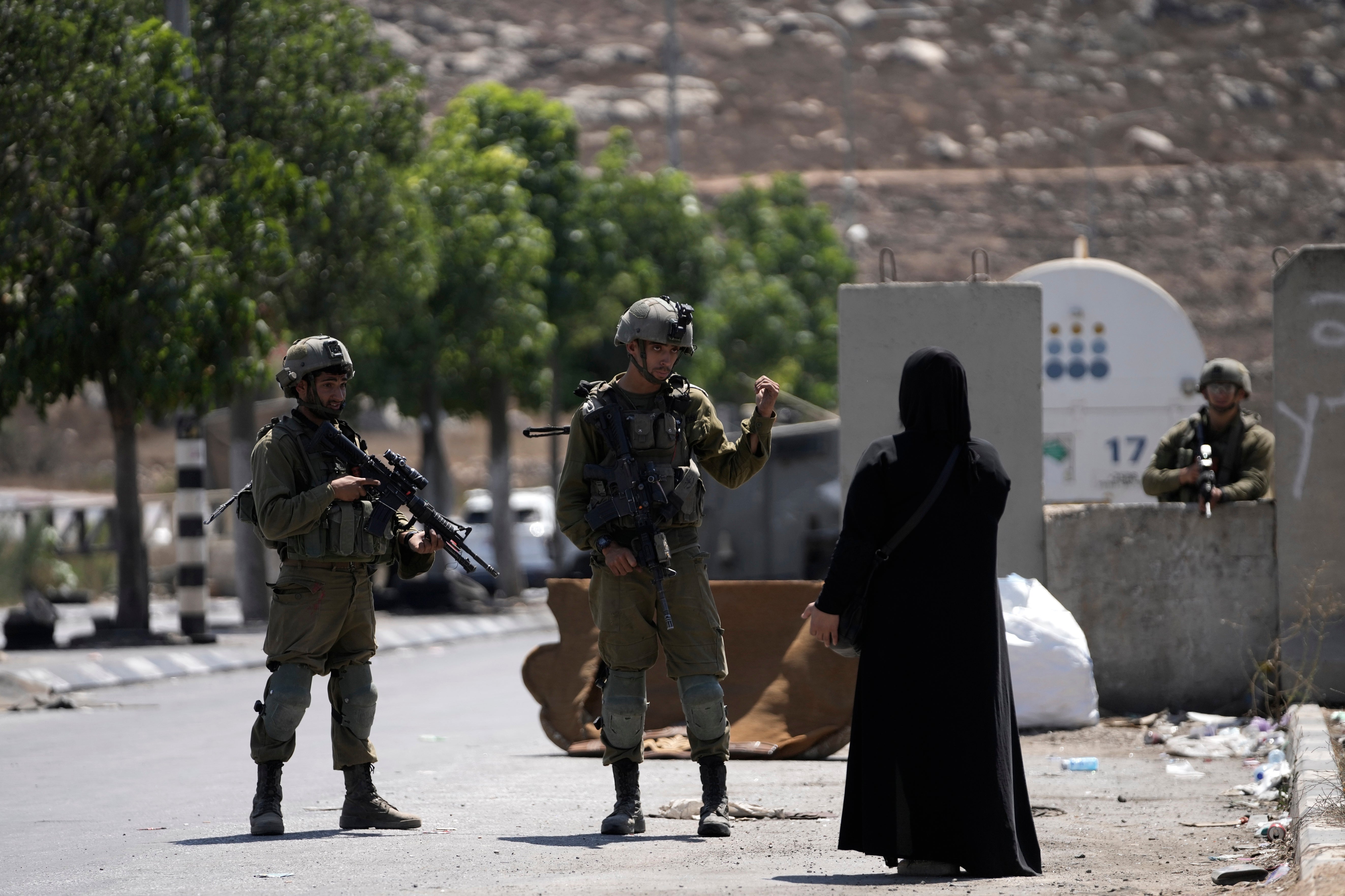 Israeli soldiers speak to a Palestinian woman near the site of an alleged car-ramming attack near Beit Hagai