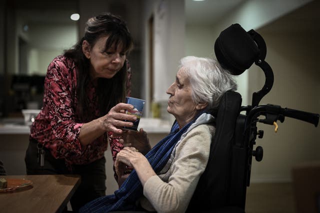 <p>A healthcare personnel (L) helps a patient with Alzheimer during lunch time in one of the living quarters of the village Landais Alzheimer site for patients with Alzheimer in Dax, south-western France on November 30, 2023</p>