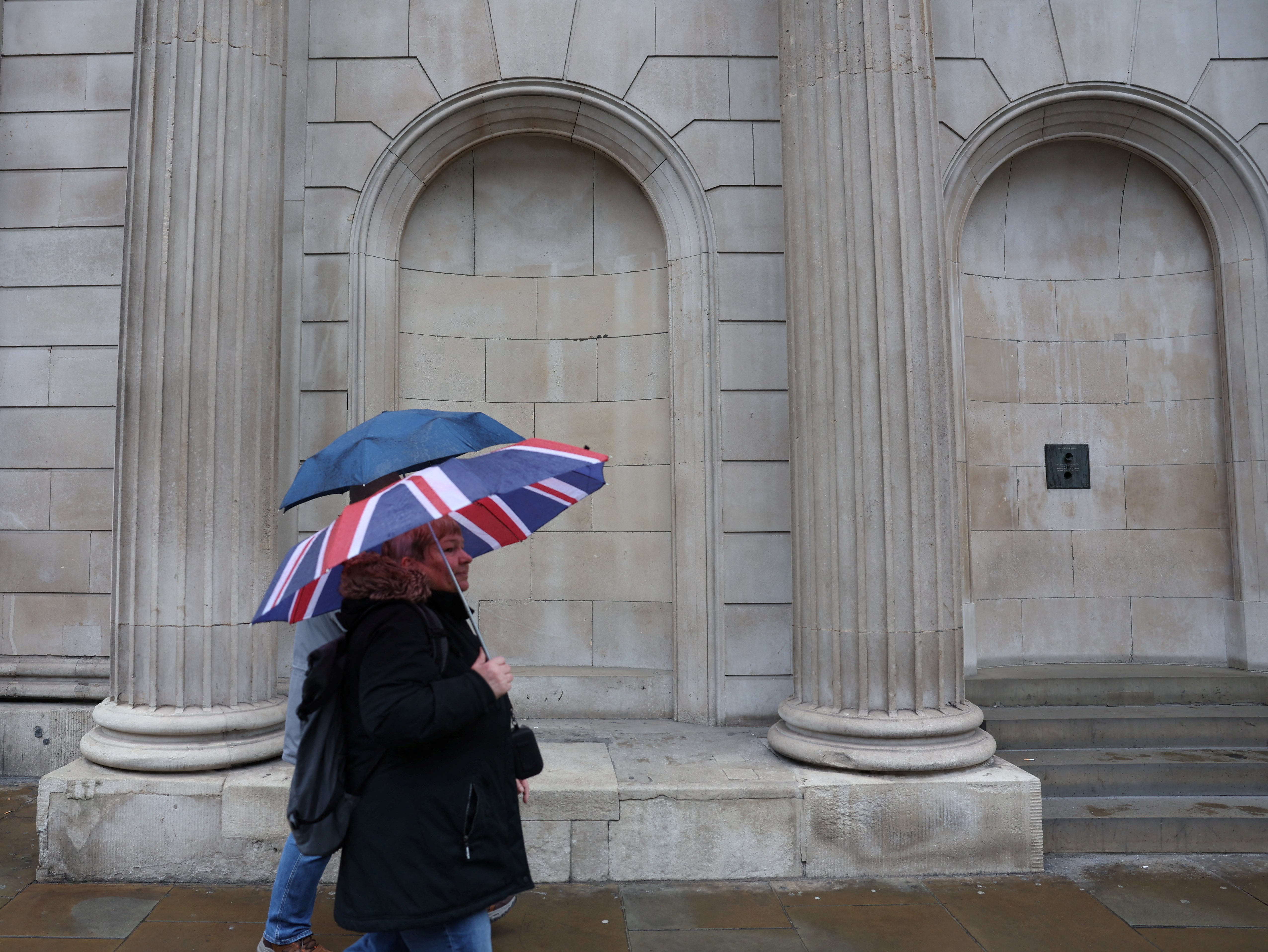 File: Tourists shelter from the rain under an Union Jack umbrella near the Bank of England in the City of London financial district in London, Britain, 13 February 2024