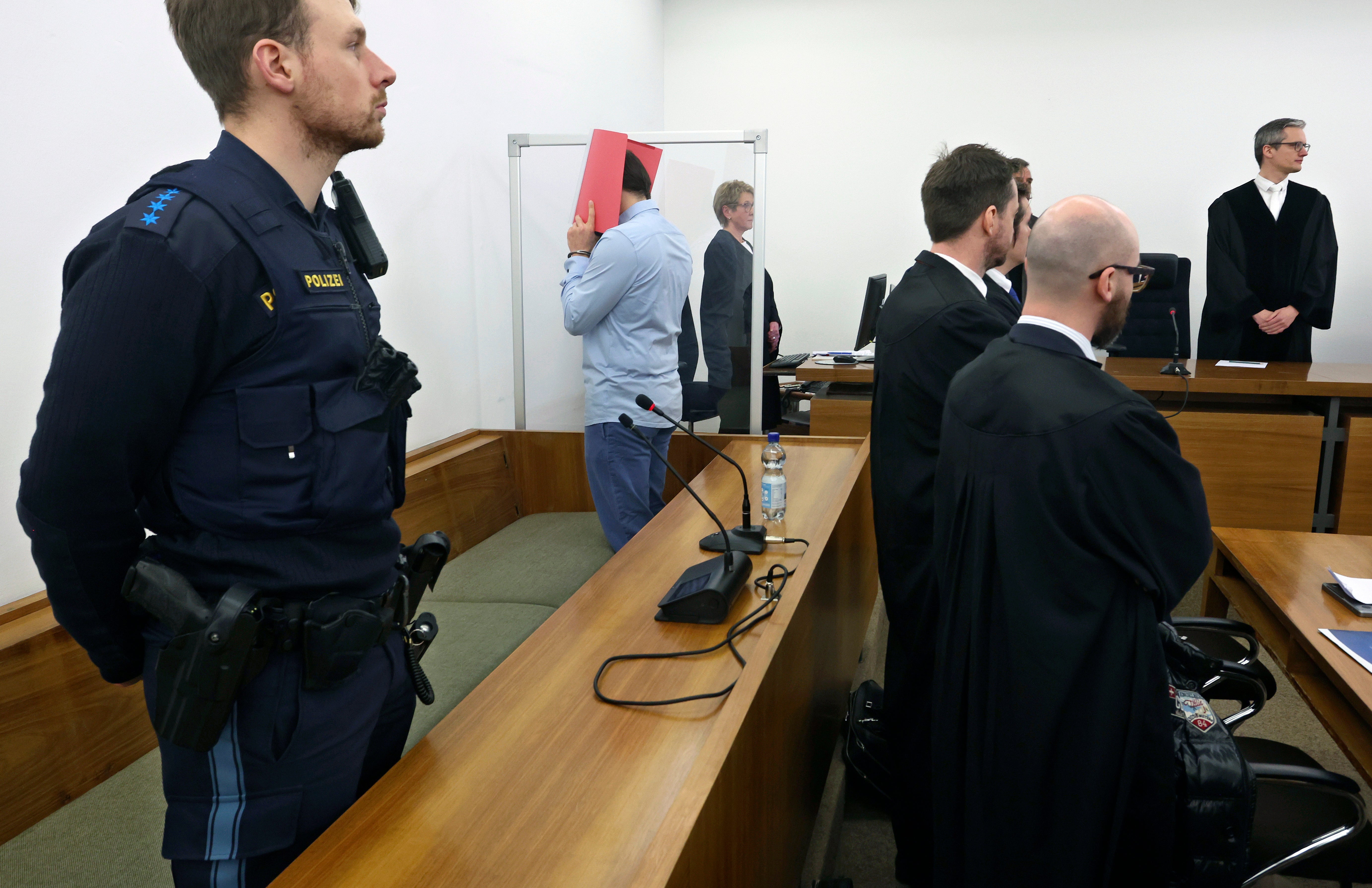 A 31-year-old American man accused of murder stands in the dock behind his lawyers in a courtroom