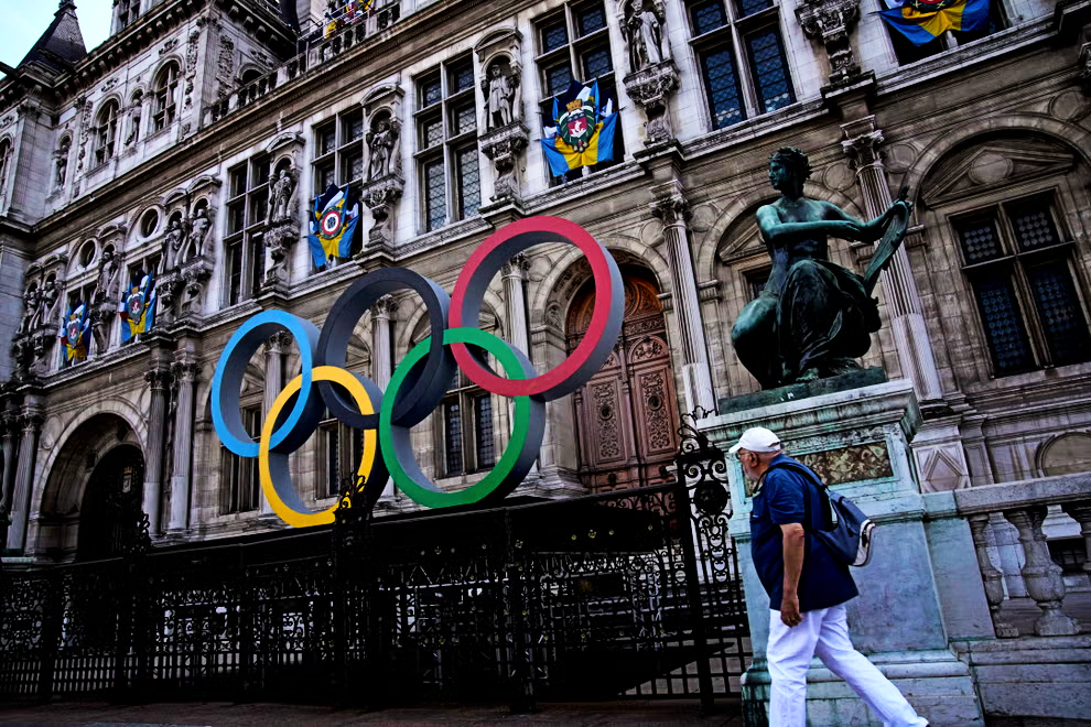 A man walks past the Olympic rings in front of the Paris City Hall