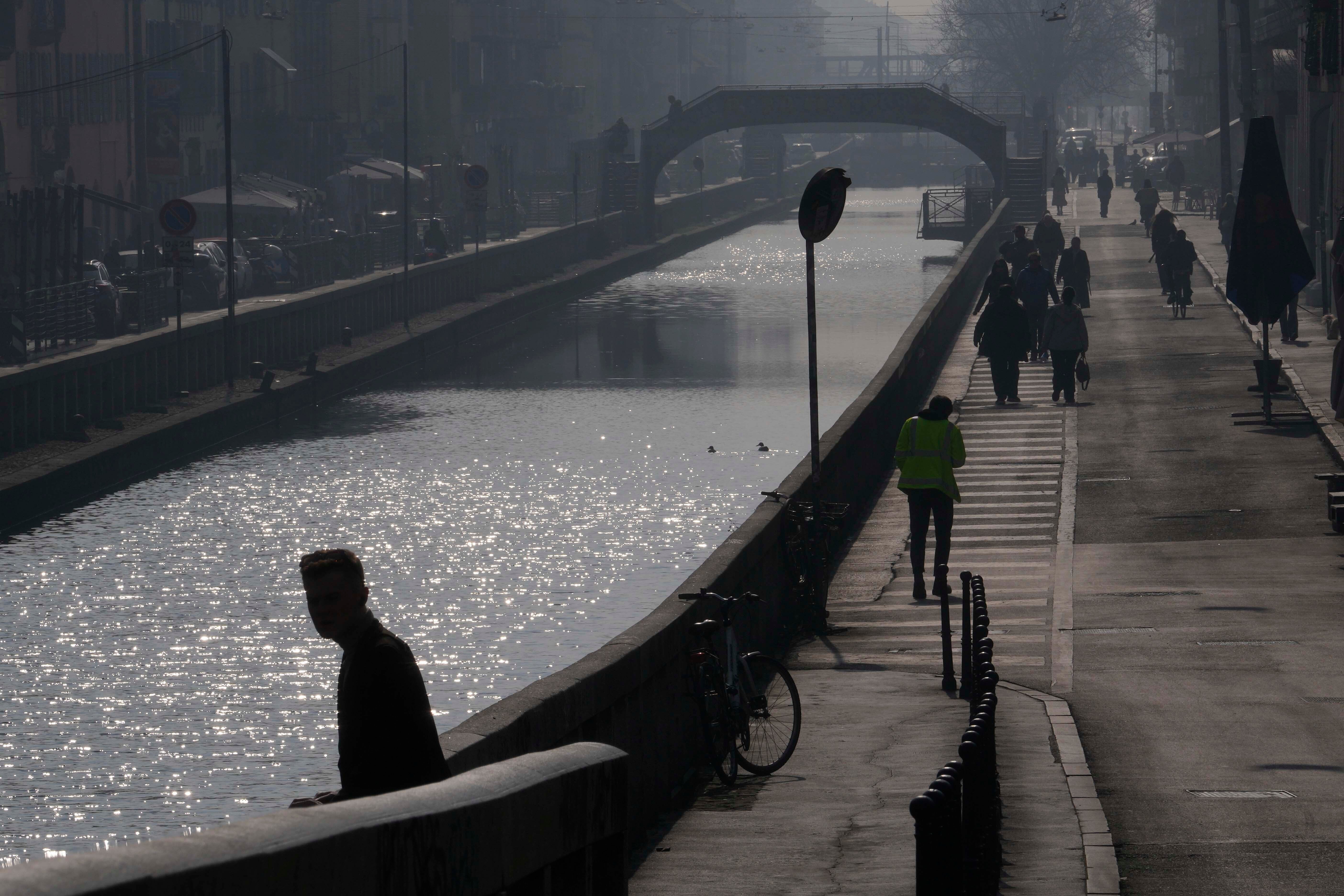 People walk along a shrouded in mist and smog Naviglio Pavese canal, in Milan