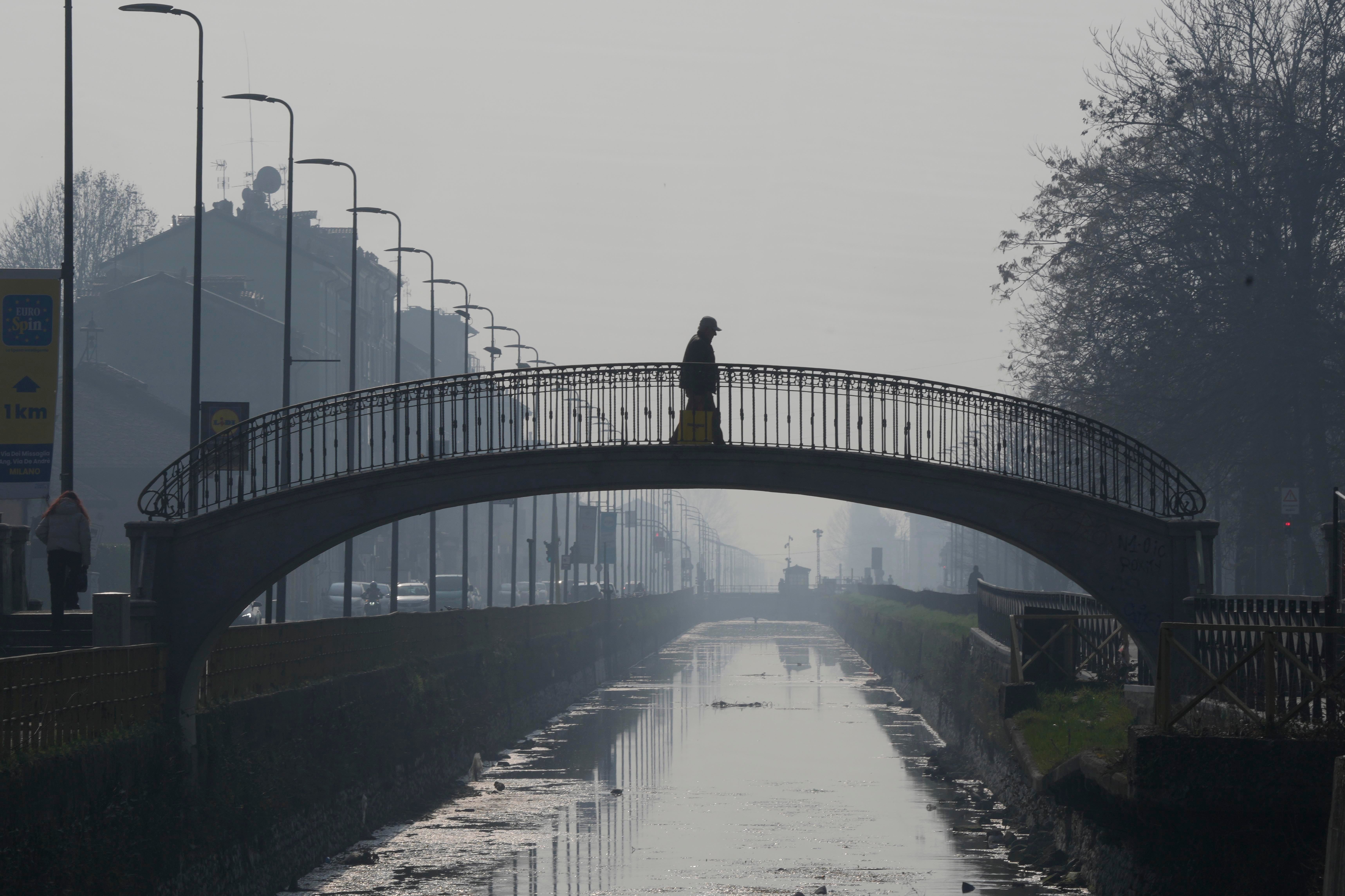A man walks on a bridge shrouded in mist and smog, at the Naviglio Pavese canal in Milan, Italy on Monday