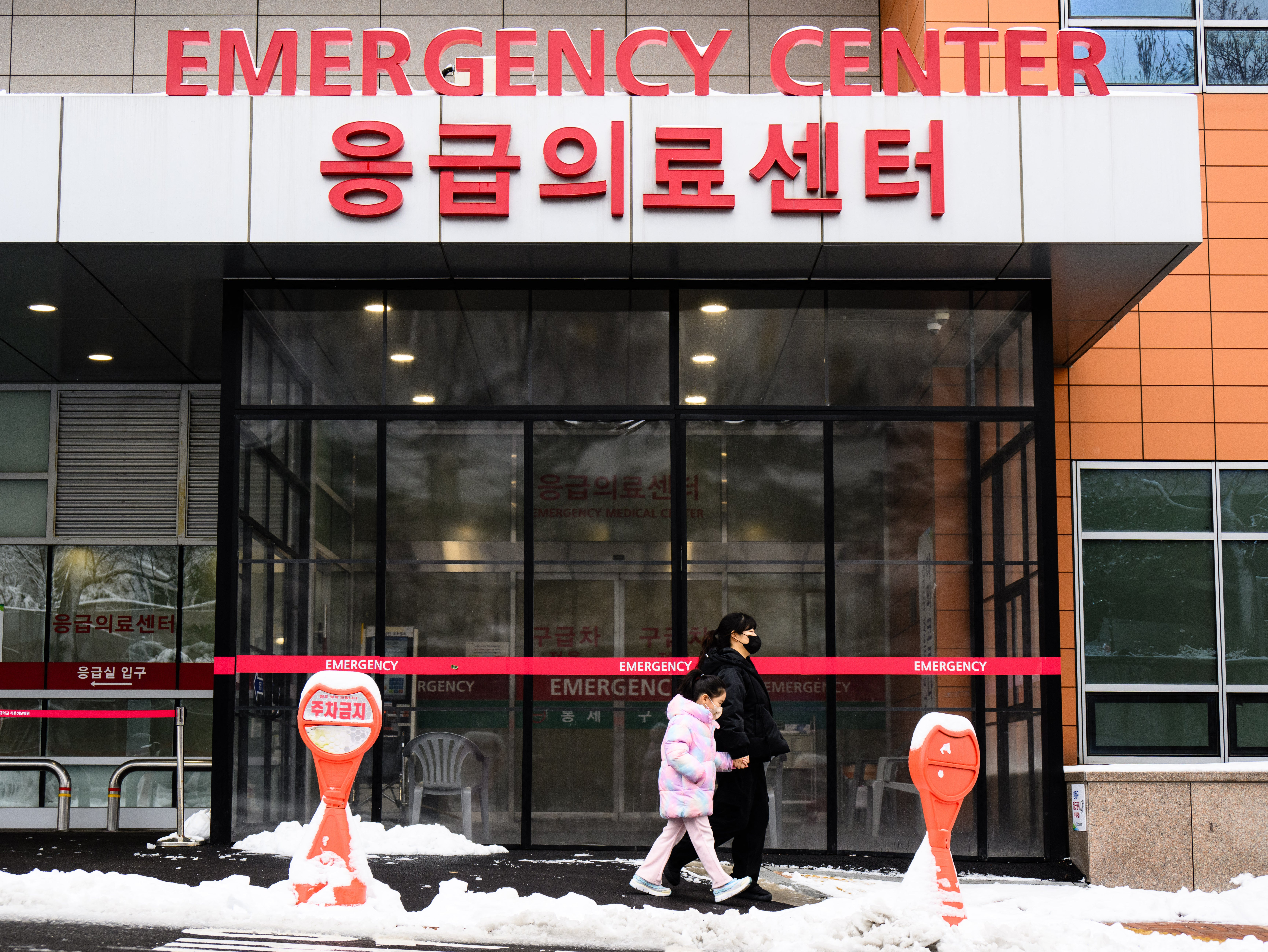 <p>A woman and a child walk outside an emergency centre of a hospital after snowfall in Seoul on 22 February 2024. - South Korean hospitals were thrown into chaos this week as thousands of trainee doctors downed tools to protest medical training reforms aimed at ending a shortage of medics</p>