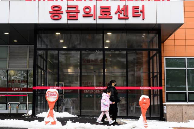 <p>A woman and a child walk outside an emergency centre of a hospital after snowfall in Seoul on 22 February 2024. - South Korean hospitals were thrown into chaos this week as thousands of trainee doctors downed tools to protest medical training reforms aimed at ending a shortage of medics</p>