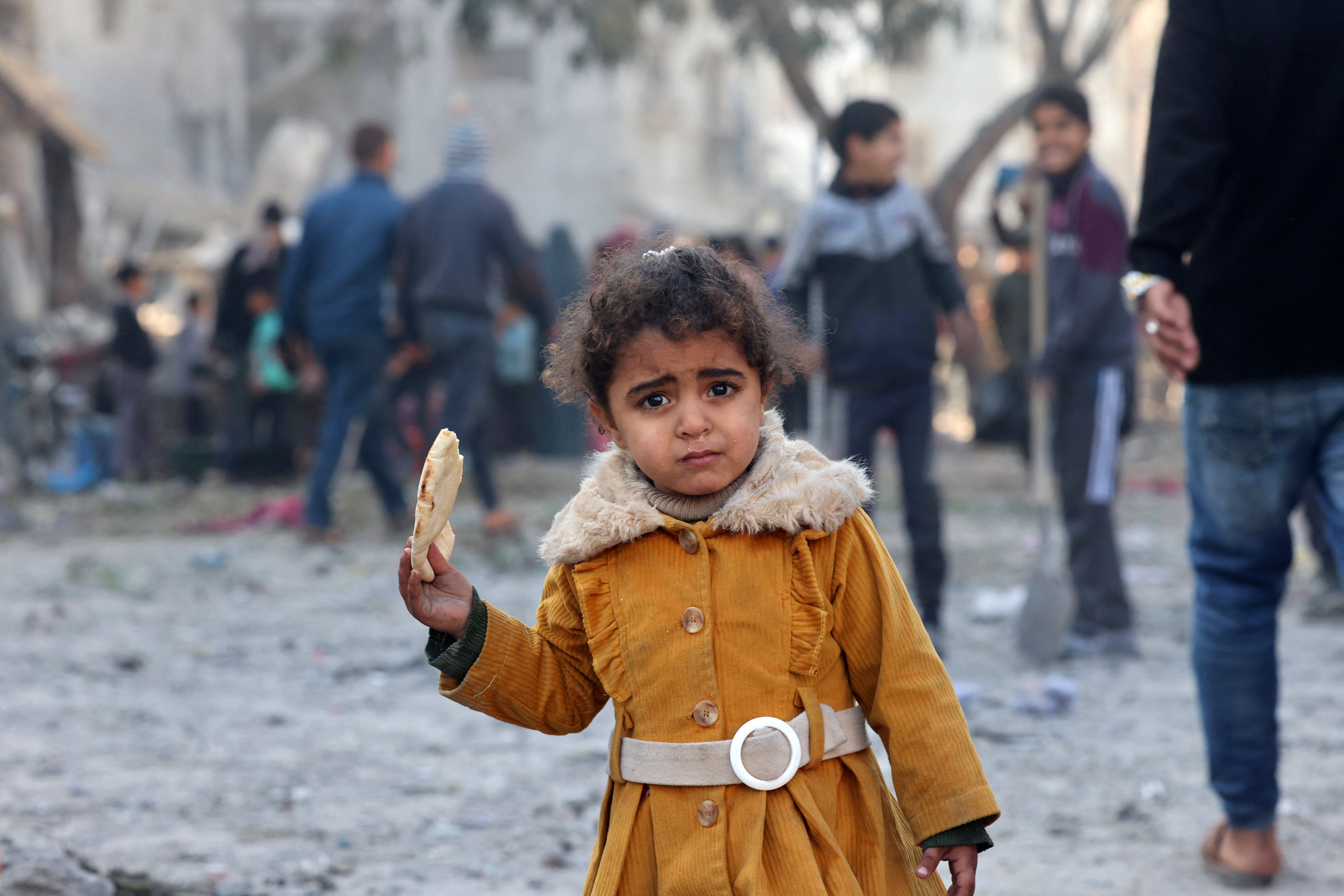 A Palestinian girl eats a piece of bread as people check debris on following overnight Israeli air strikes in Rafah refugee camp in the southern Gaza strip