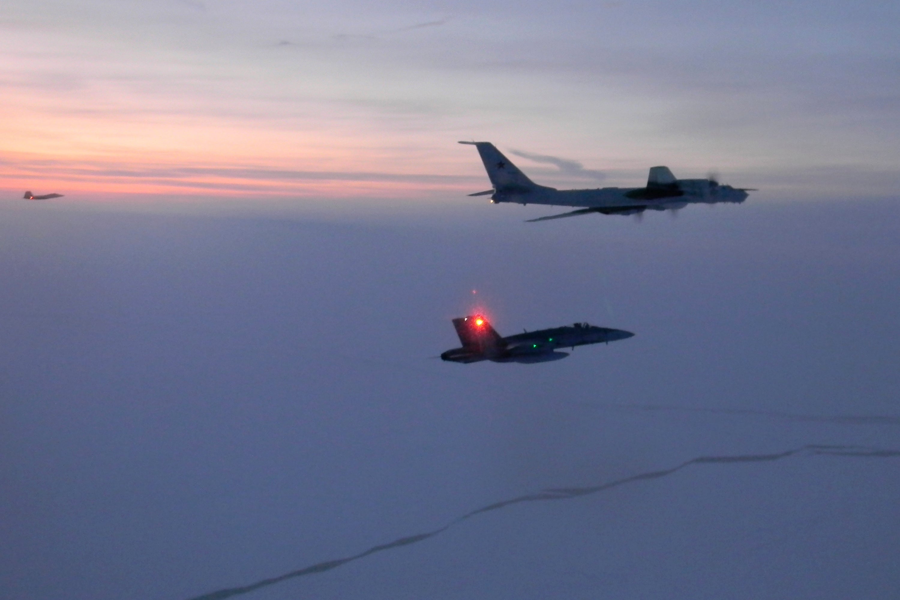 A Russian Tu-142 maritime reconnaissance aircraft, top, being intercepted near the Alaska coastline