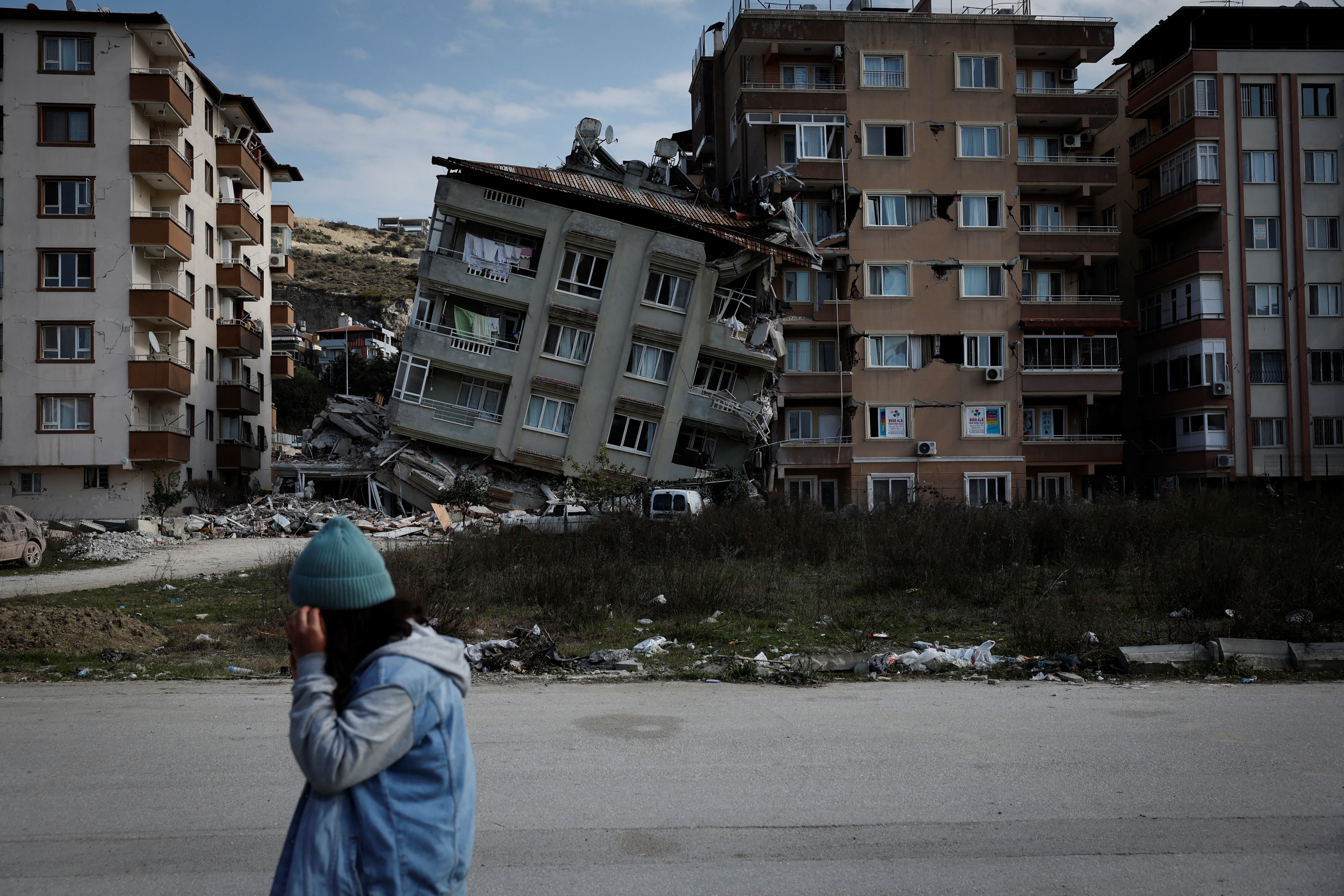 A woman walks past damaged buildings and rubble in the aftermath of a deadly earthquake, in Antakya