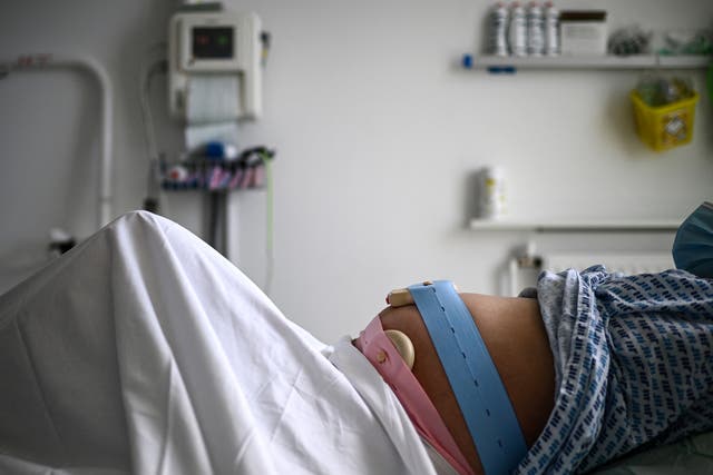 A pregnant woman lies on her bed with monitoring devices placed on her belly as she gets ready before delivering her child at the maternity ward of a hospital in Paris on June 29, 2022