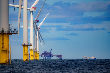 <p>Wind turbines in the North sea are photographed with an oil platform in the distance</p>