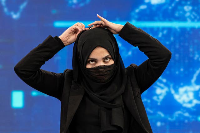 <p>A female presenter for TOLOnews covers her face during a live broadcast at Tolo TV station in Kabul</p>