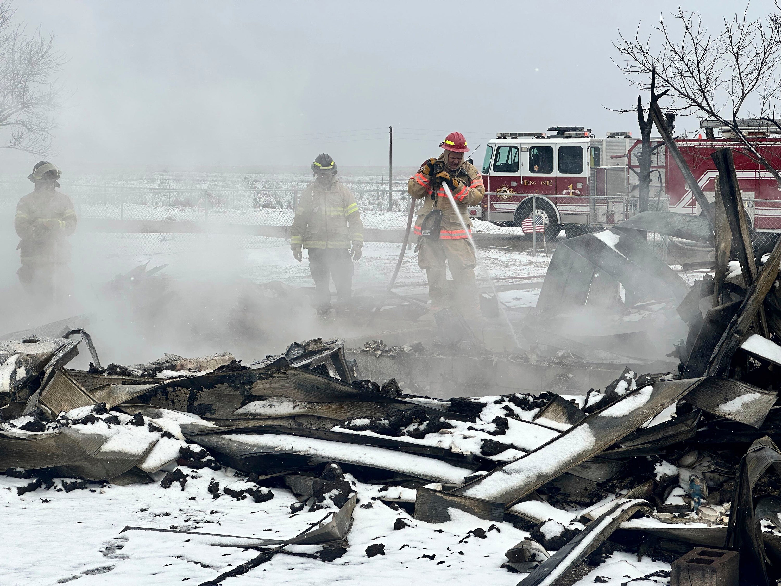 Firefighters extinguish flames in Stinnett, Texas on Thursday as snow covers the ground