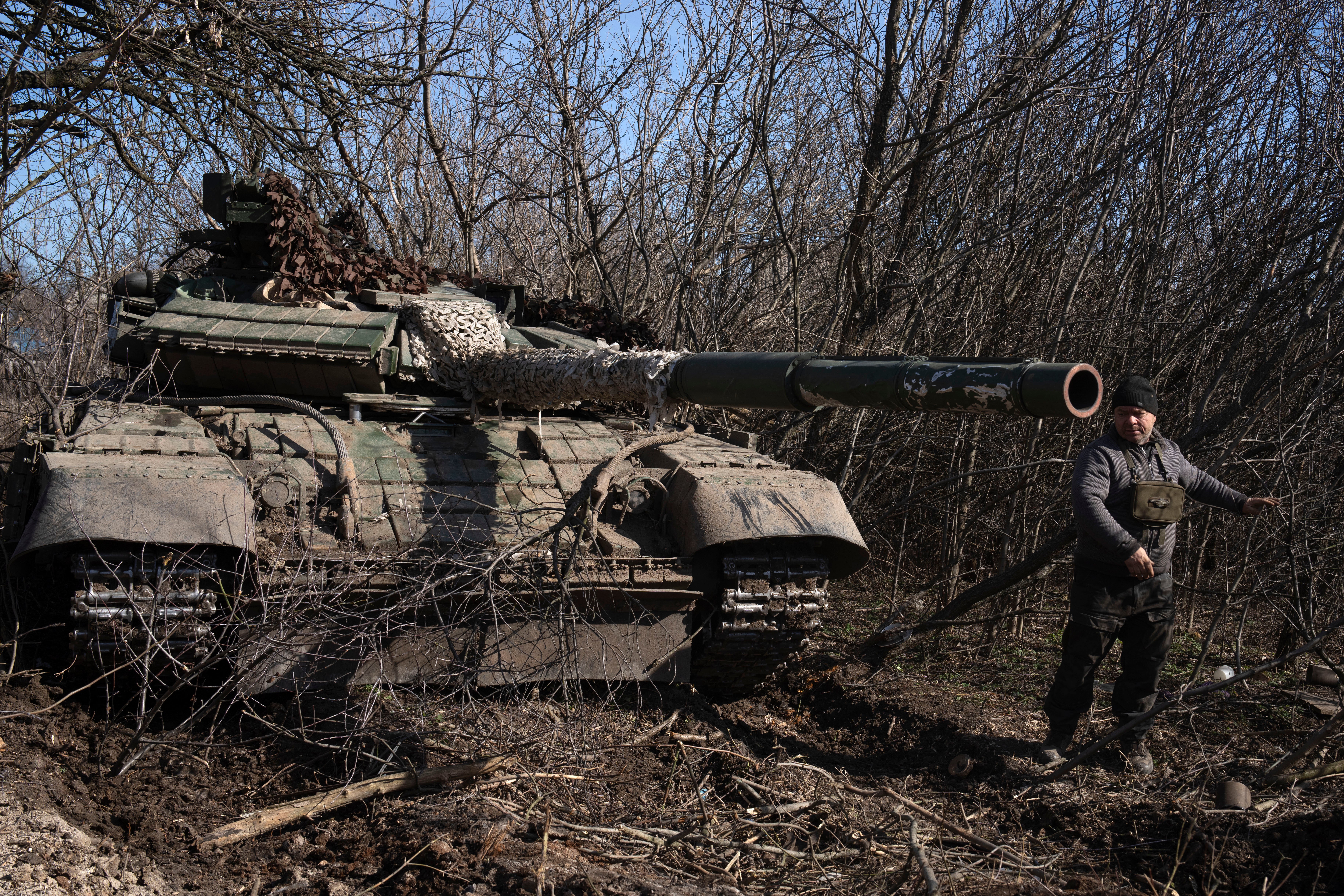 A tanker of Ukraine's 17th Tank Brigade removes tree branches from his T-64 tank in Chasiv Yar