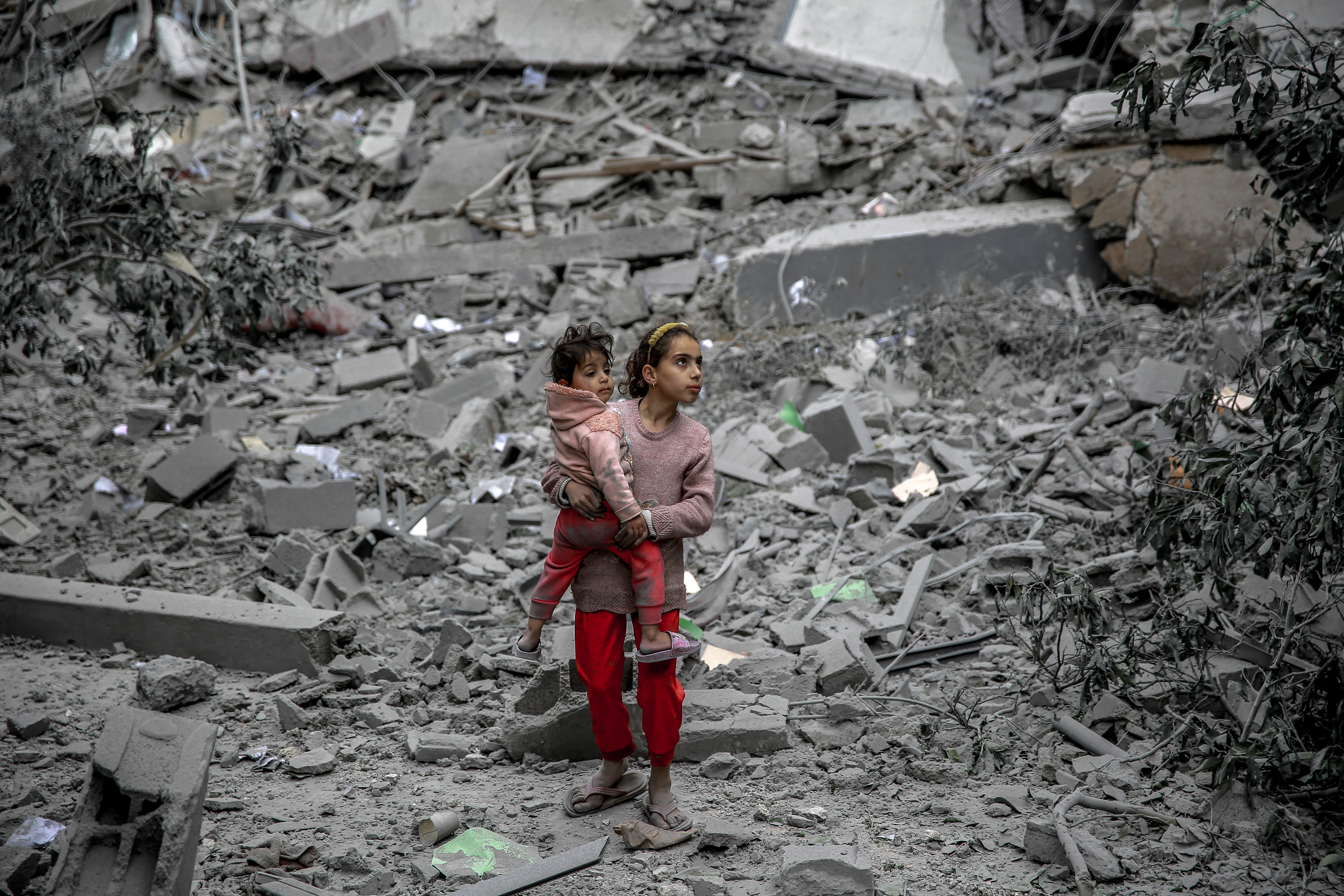 A Palestinian girl carries a child through the rubble of houses destroyed by Israeli bombardment in Gaza City on March 3, 2024