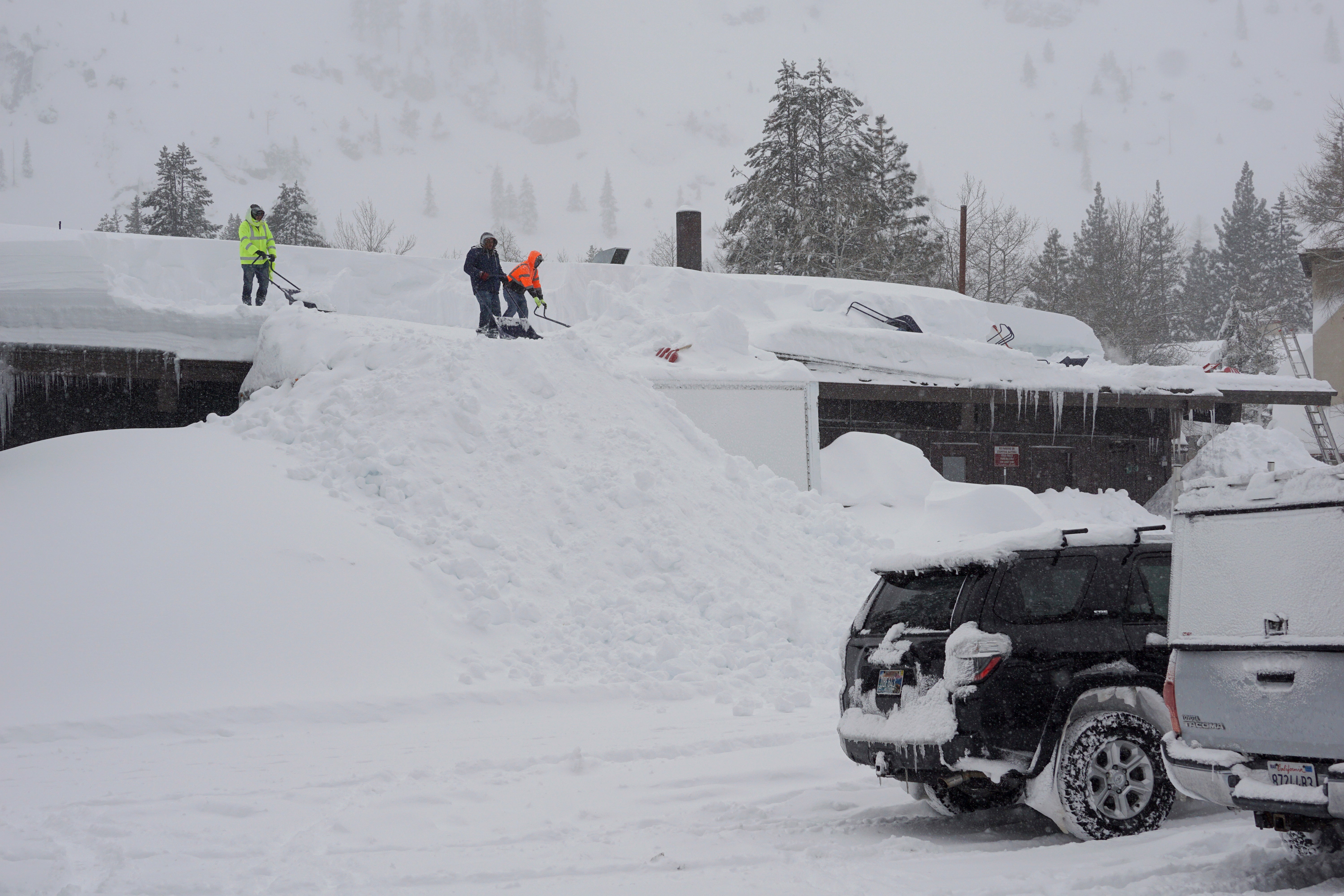 Workers clear snow off the roof of a building during a blizzard Sunday, March 3, 2024, in Olympic Valley, California