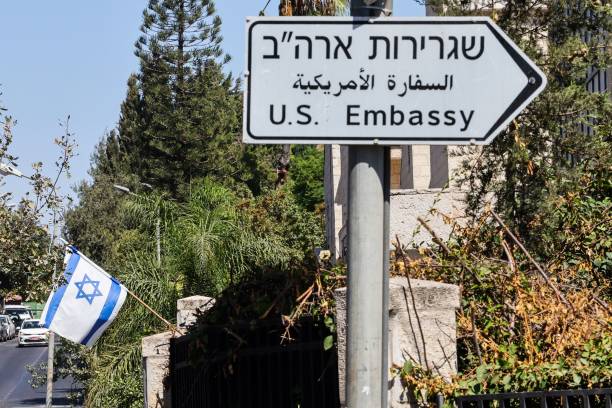 An Israeli flag is displayed in front of a building near a road sign for the US embassy in Jerusalem