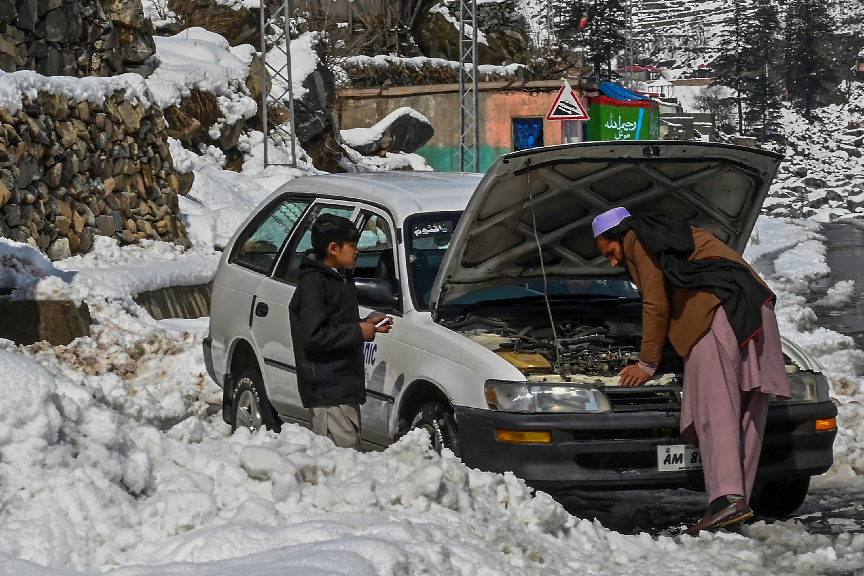 A man fixes his car along a snow laden street in Kalam on 4 March 2024