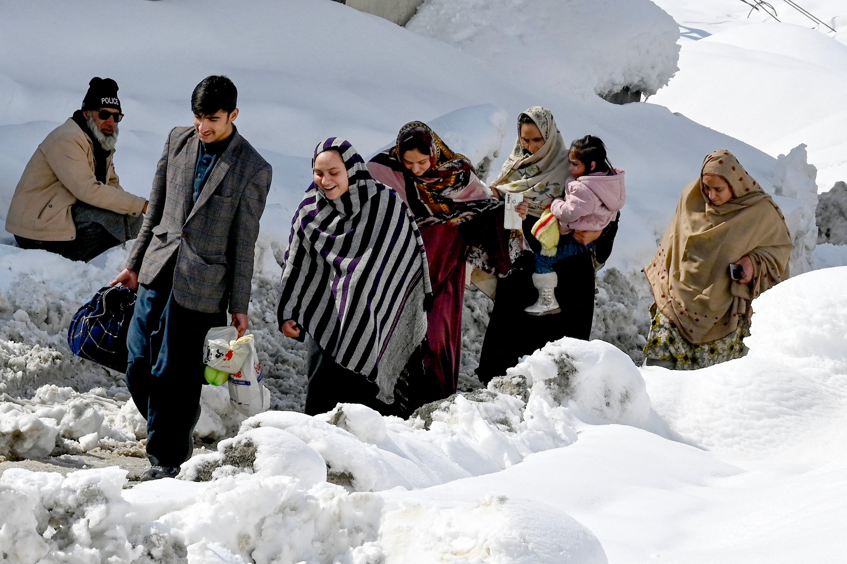 People walk amid a snow laden street in Kalam on 4 March 2024