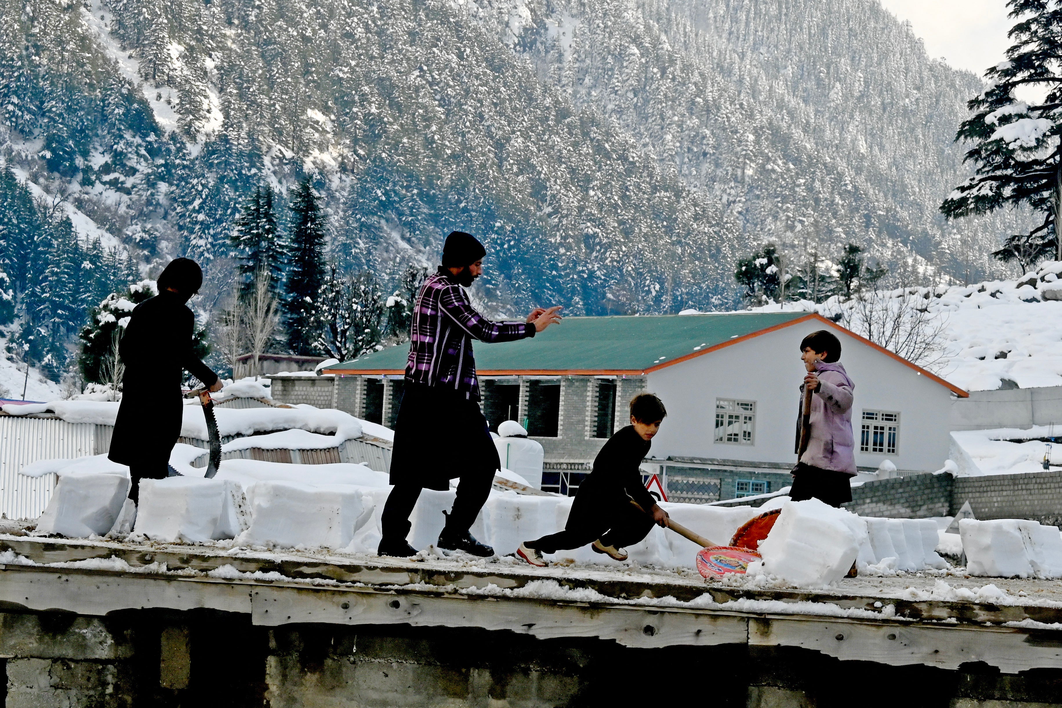 Boys remove snow from the roof of their house in Kalam on 4 March 2024