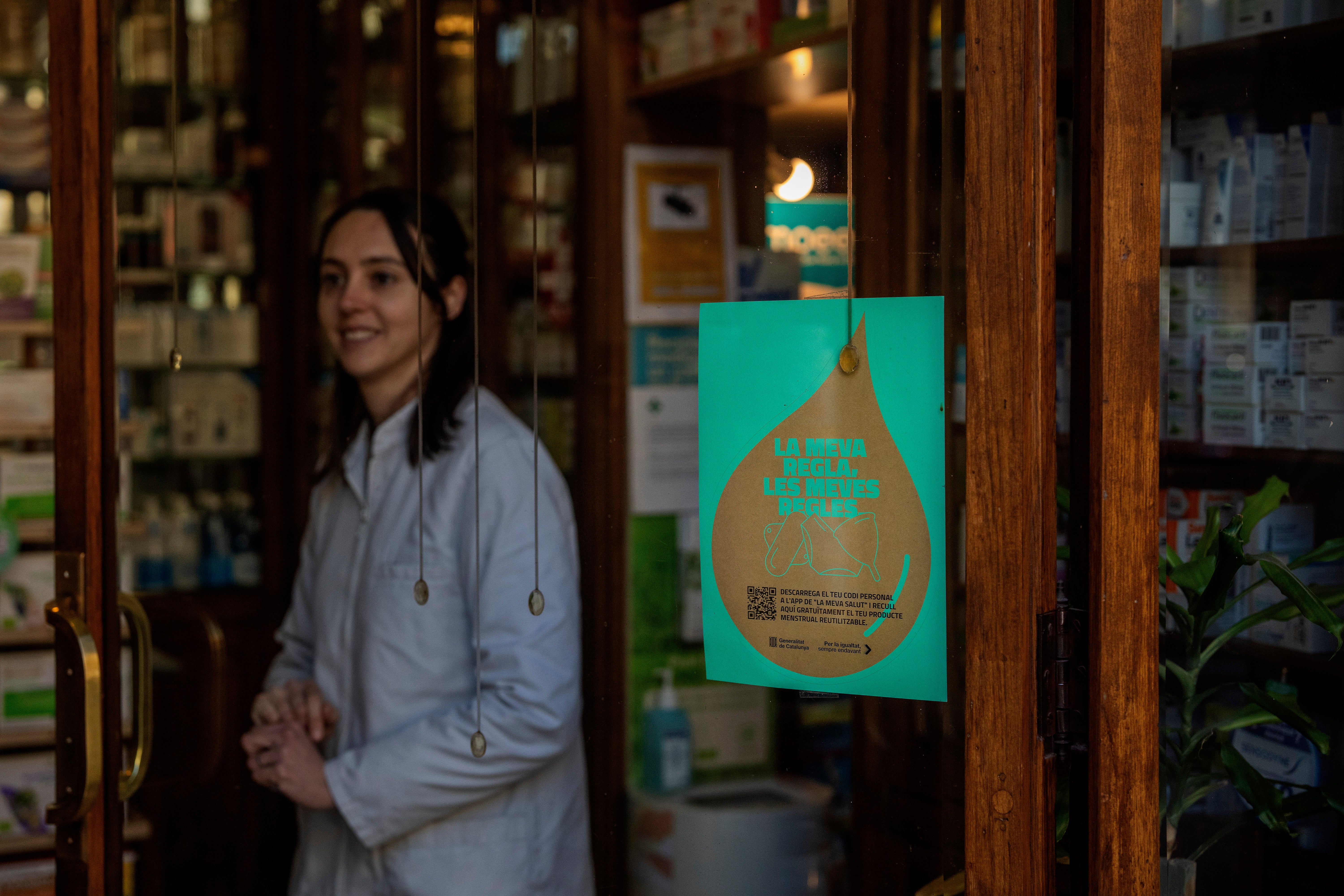 A pharmacist waits for customers next to windows where an advertisement for the new campaign