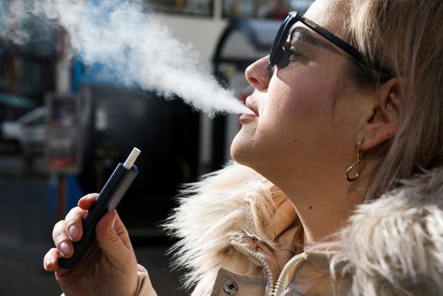 <p>A woman holds an e-cigarette as she vapes on a street in Manchester</p>