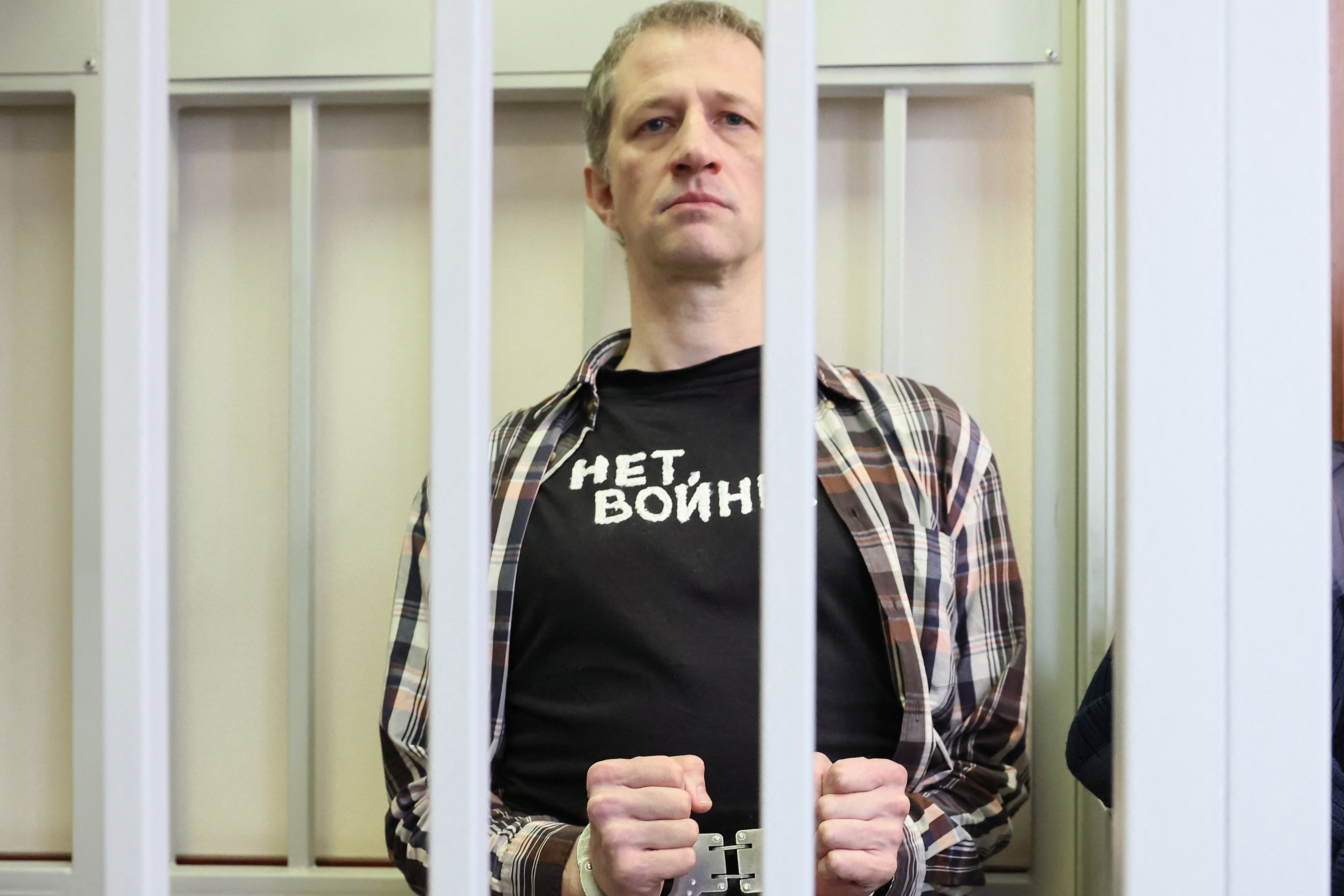 Russian journalist Roman Ivanov, wearing a T-shirt that says ‘No war,’ stands inside a defendants’ cage