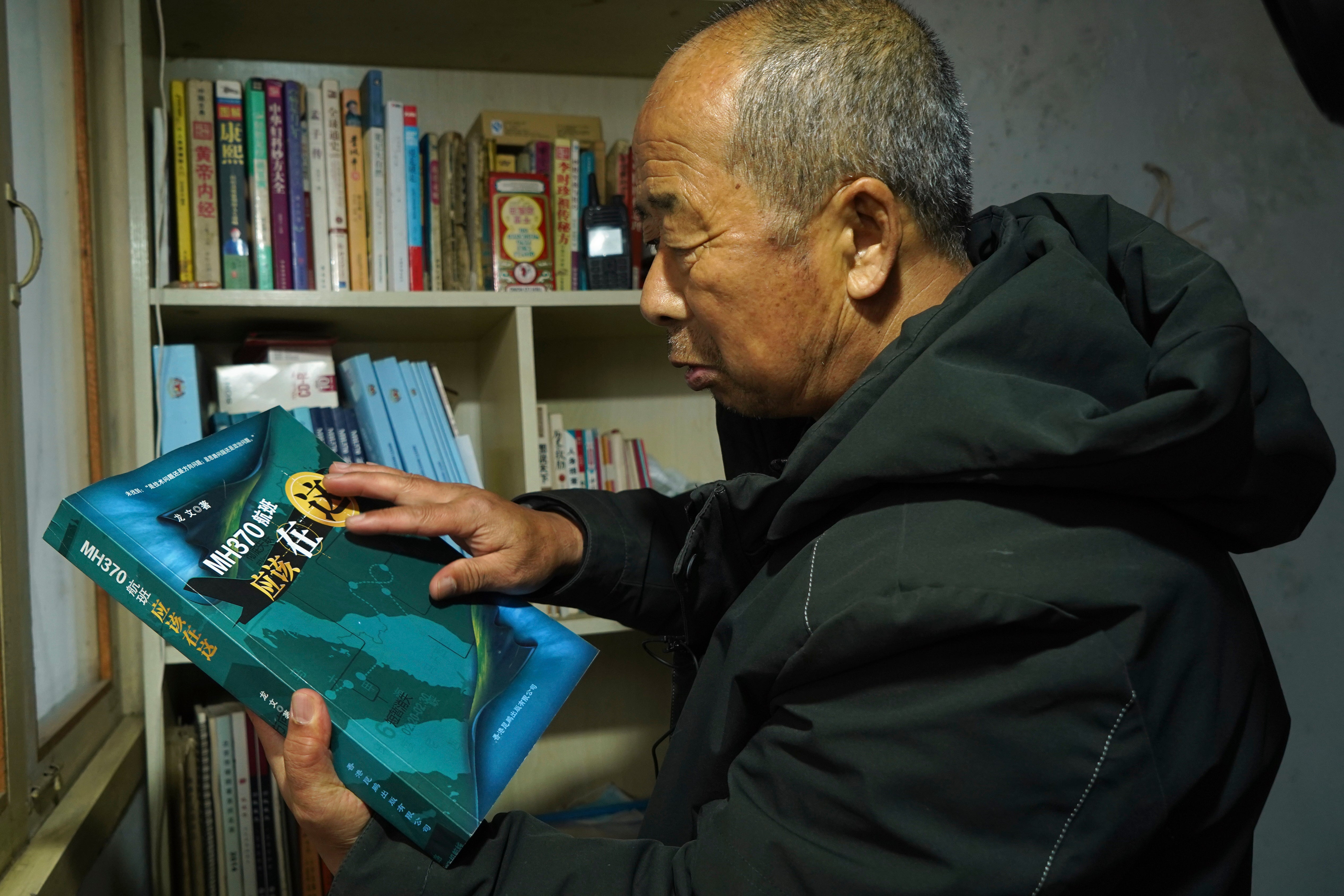 Chinese farmer Li Eryou looks at a book written about the missing Malaysia Airlines MH370 flight from a bookshelf of his son's former room at a village in Handan in northern China's Hebei province