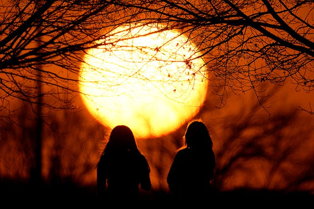 <p>People watch the sunset at a park on an unseasonably warm day in Kansas City</p>